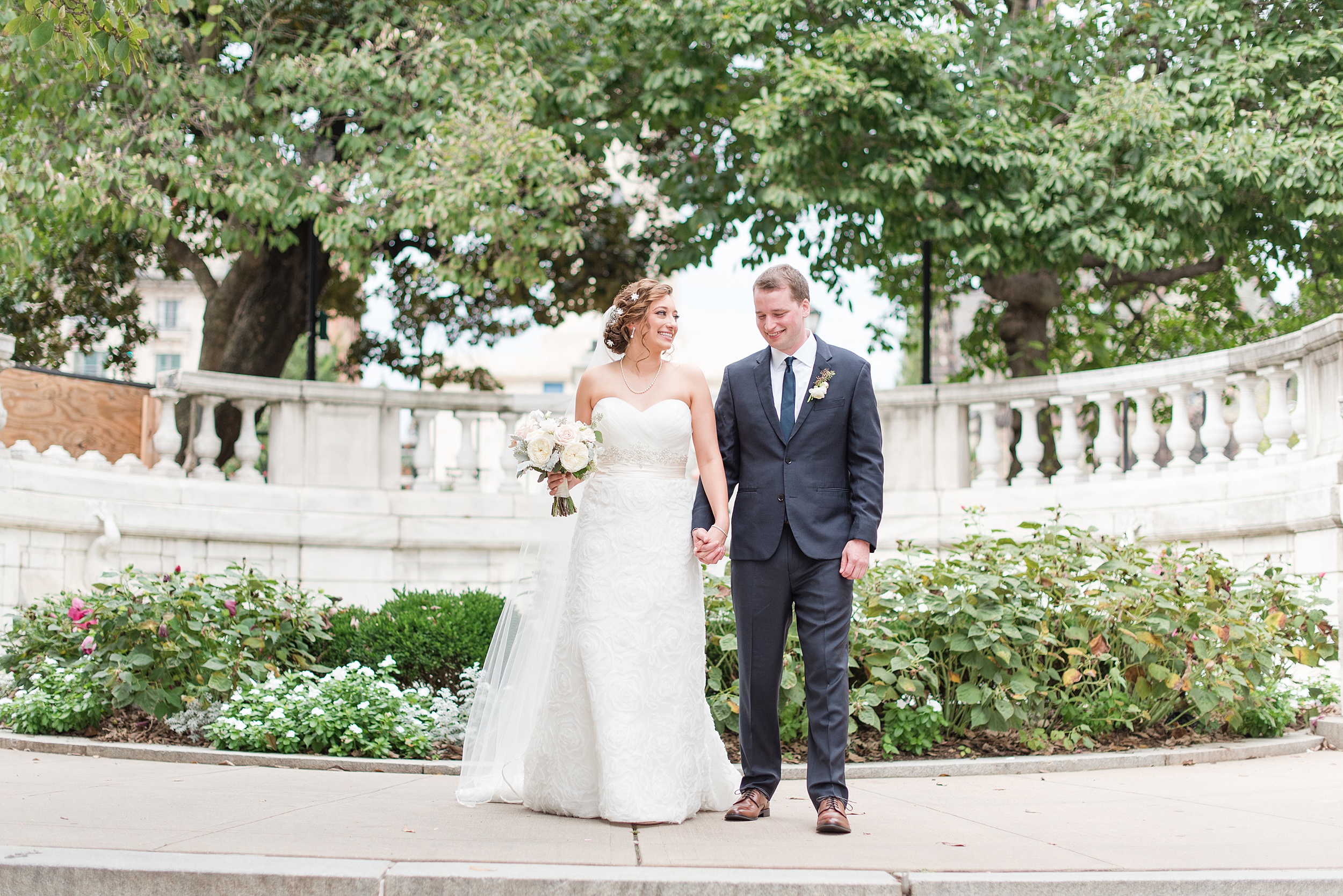 Newlyweds walk on a sidewalk in a garden holding hands at one of the beautiful Frederick Wedding Venues