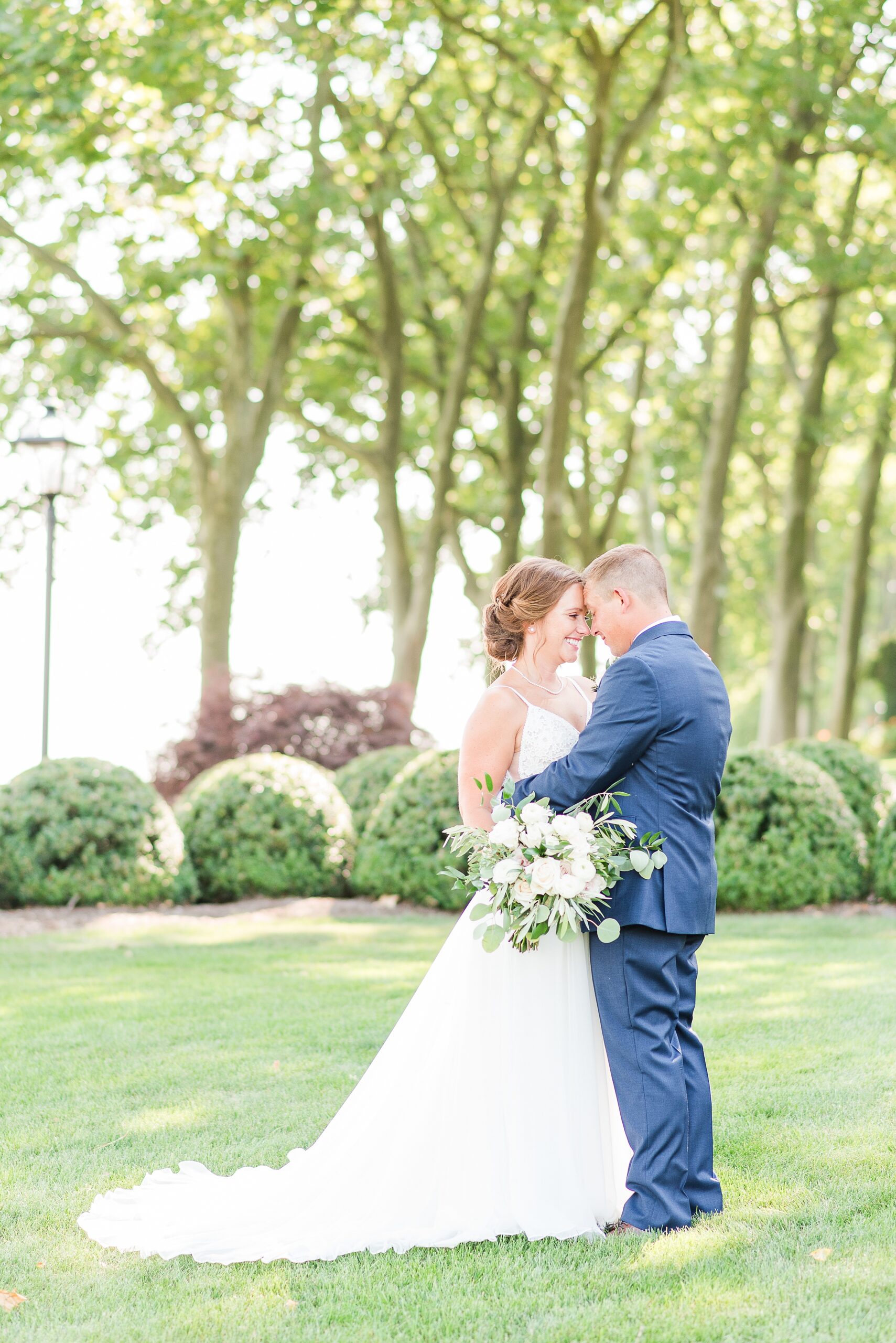 Newlyweds stand in a lawn hugging and touching foreheads at their grey rock mansion wedding