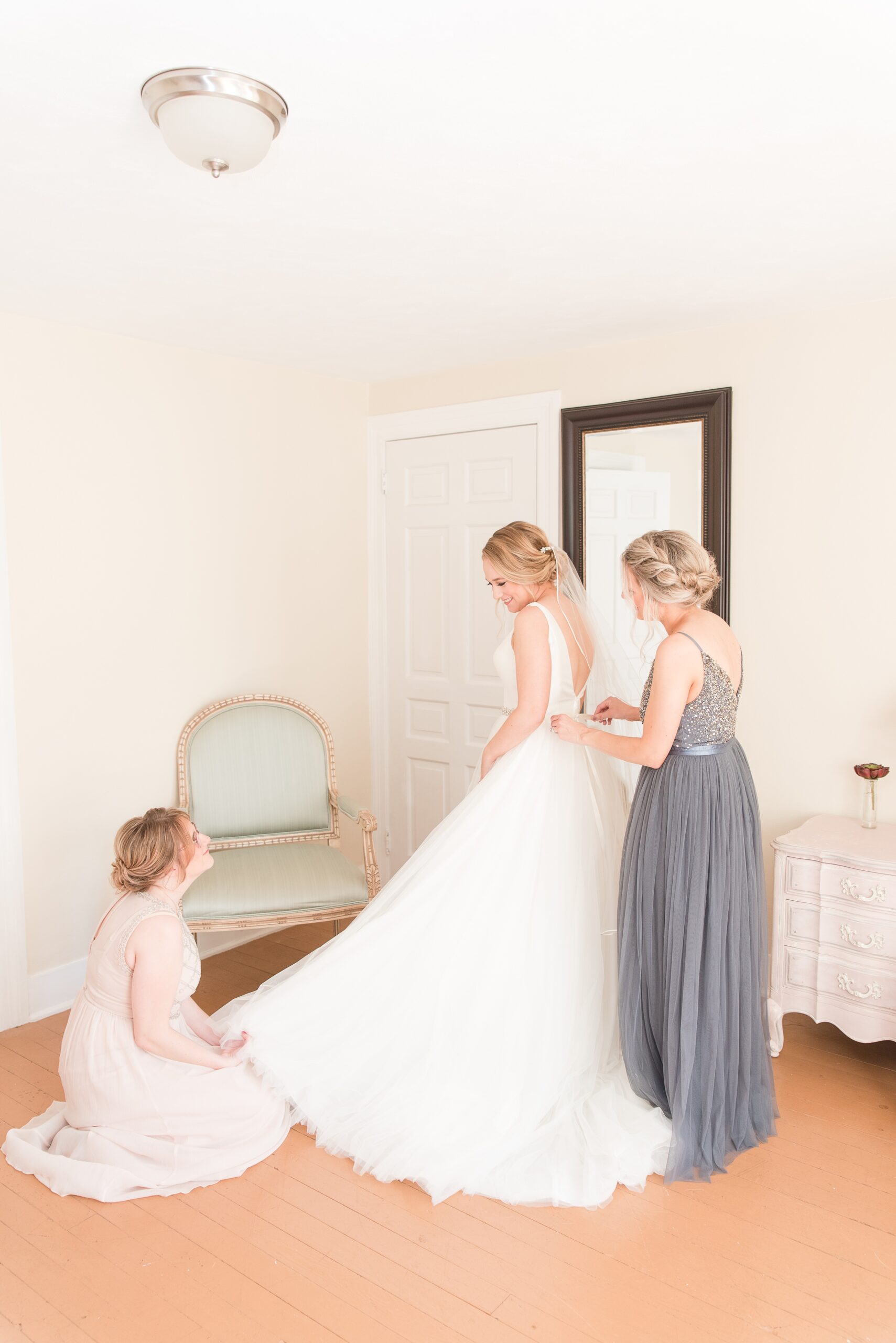 A mom and bridesmaid help a bride get into her dress