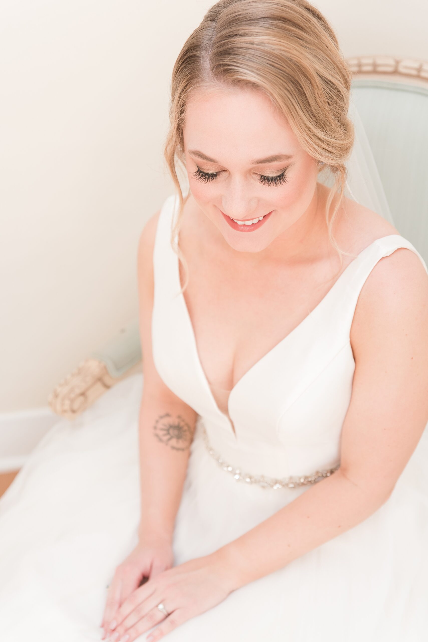 A bride sits in a chair smiling in her dress