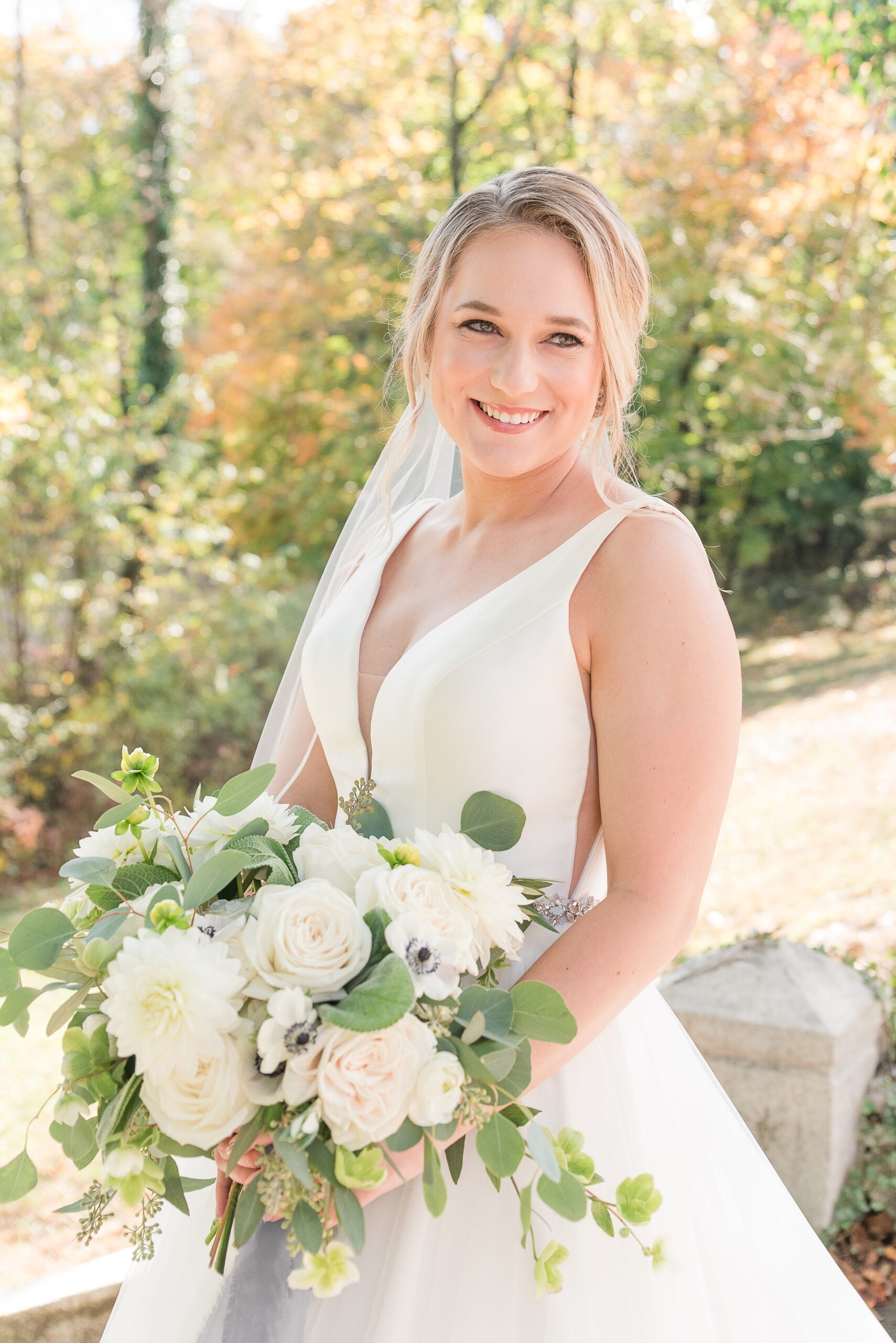 A bride smiles over her shoulder while standing in a garden holding her white rose bouquet