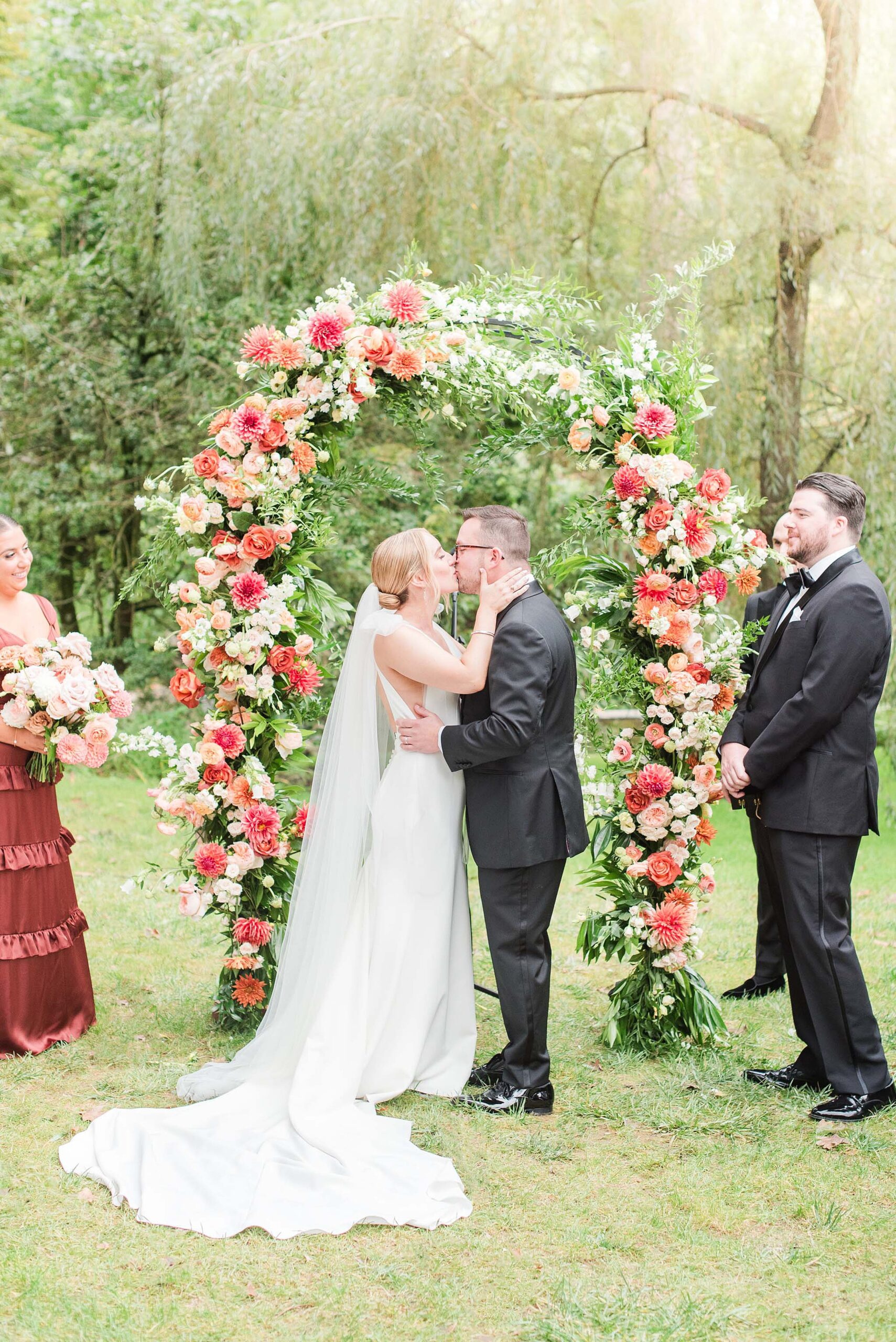 Newlyweds kiss under a colorful floral wedding arch at their outdoor Hunt Valley Country Club Wedding ceremony