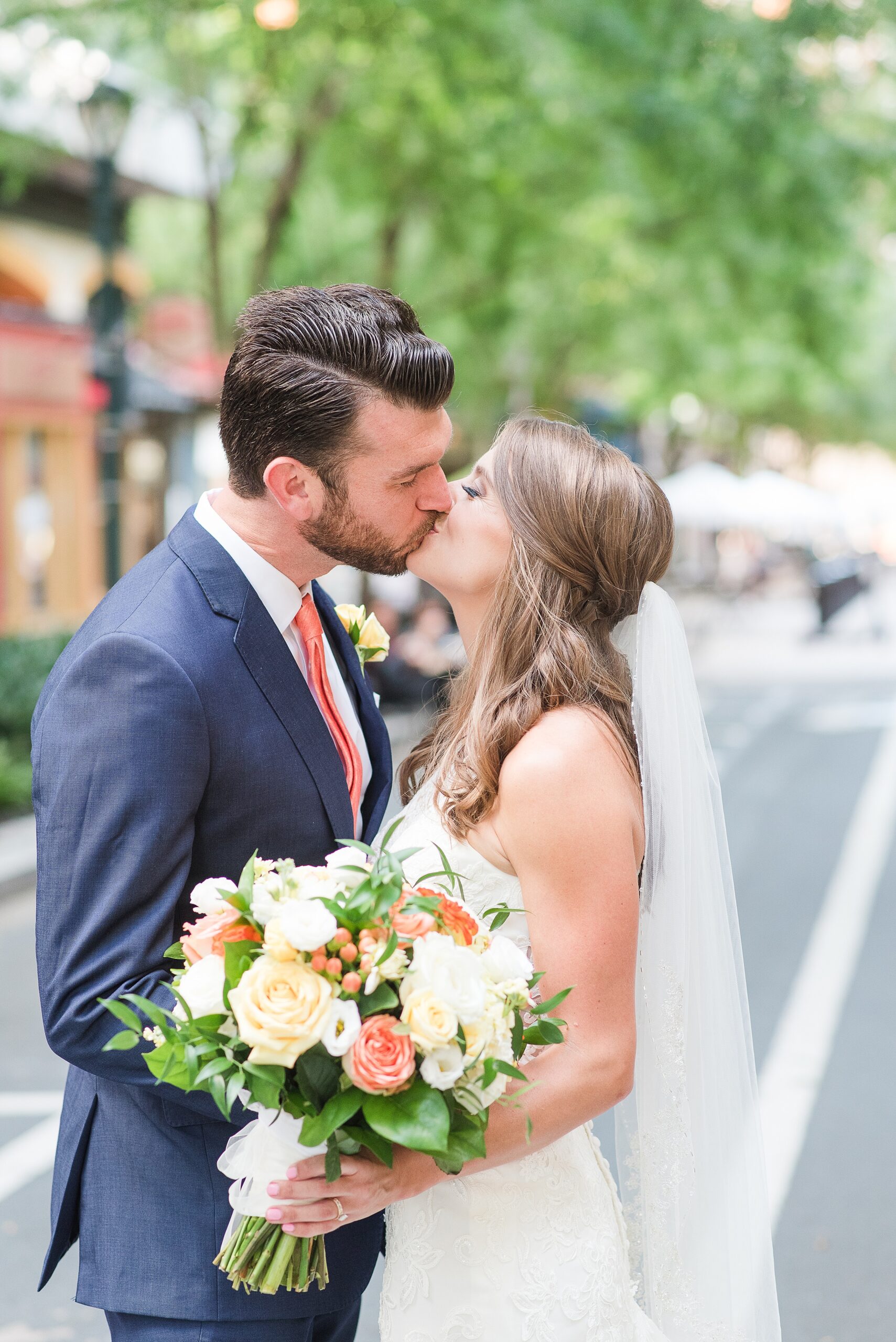 Newlyweds kiss while standing in a street and holding a large bouquet at their Hunt Valley Country Club Wedding