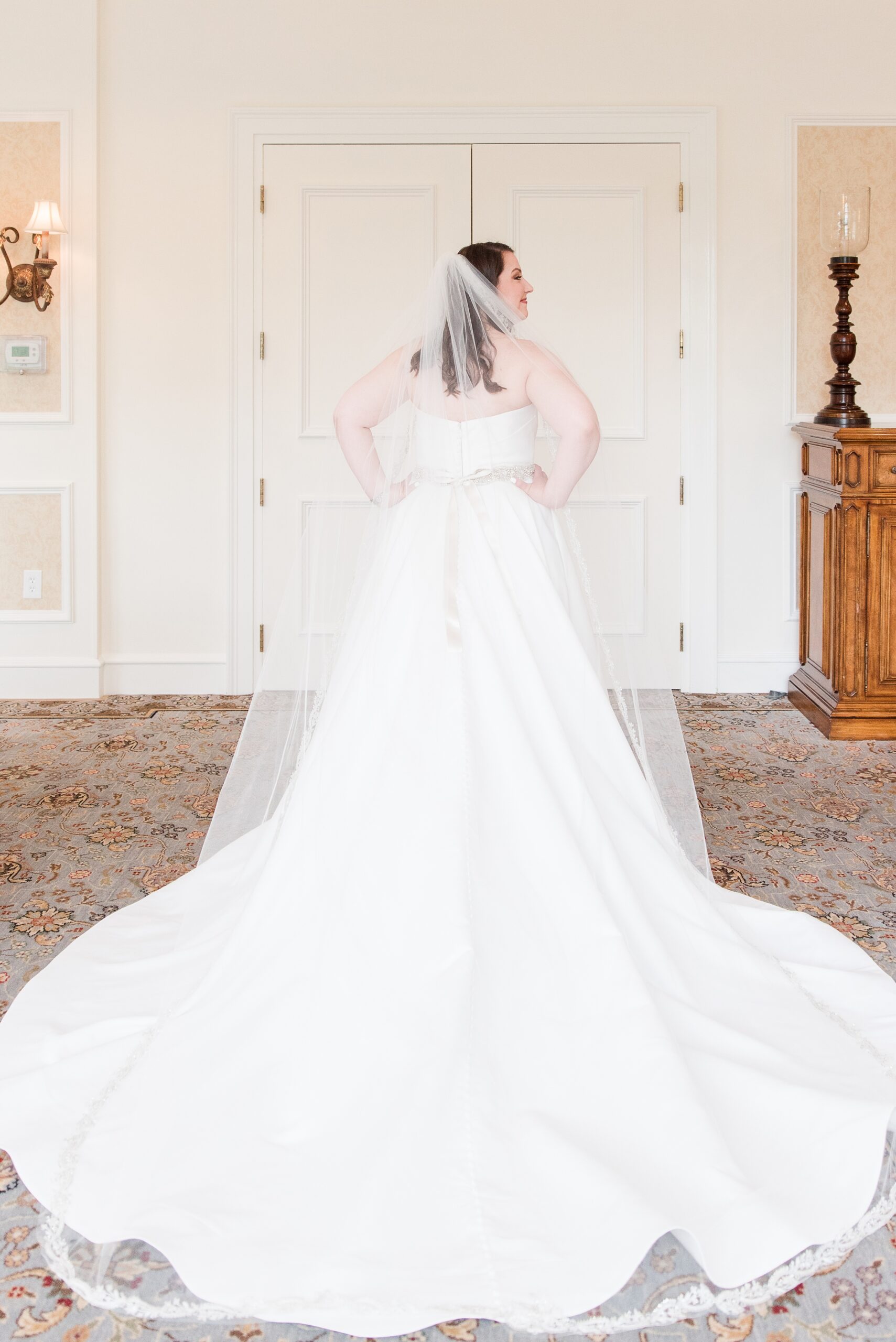 A bride proudly shows off her long train and veil in the getting ready room