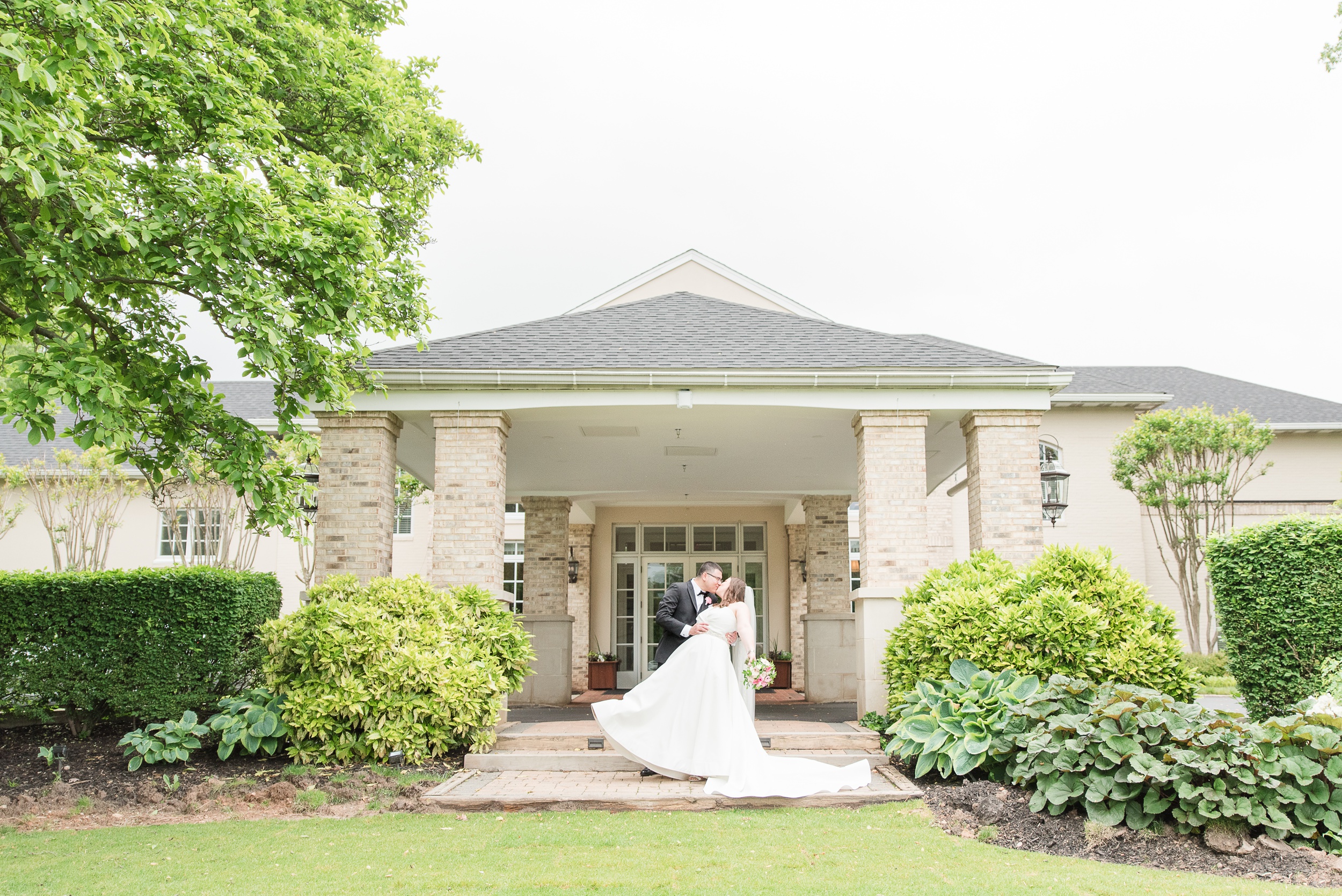 A groom dips his bride for a kiss on the front entrance garden of the Manor Country Club Wedding venue