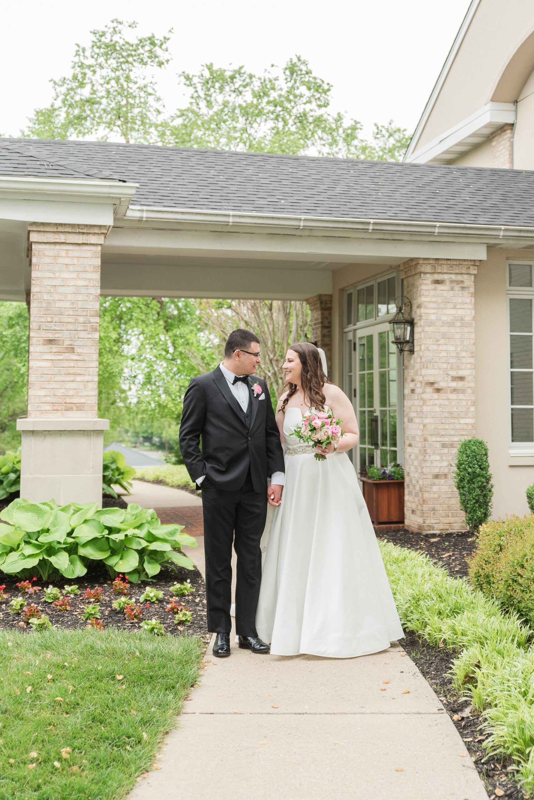 Newlyweds smile at each other while walking down a garden sidewalk