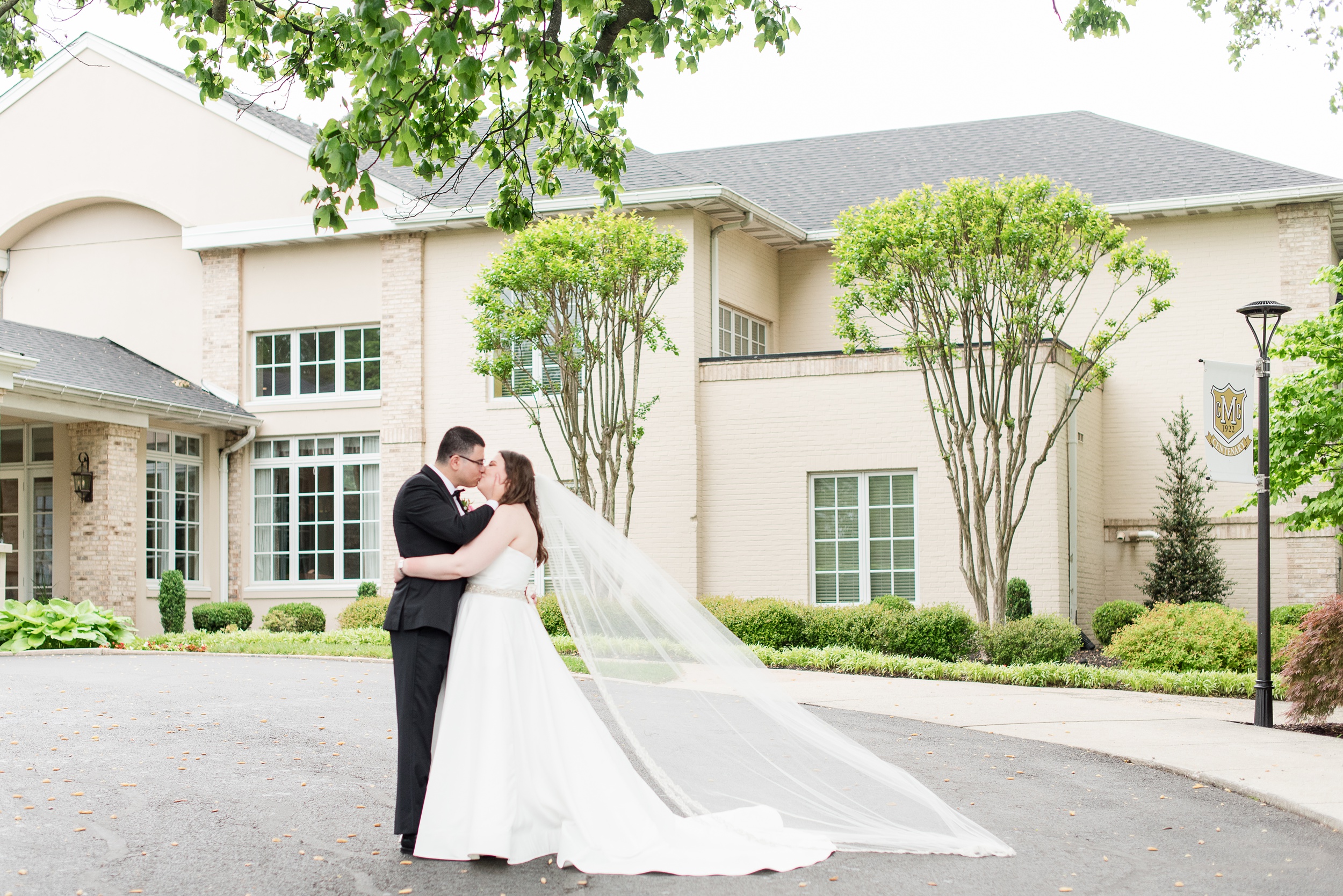 Newlyweds kiss while the veil blows in the wind in the driveway of their Manor Country Club Wedding