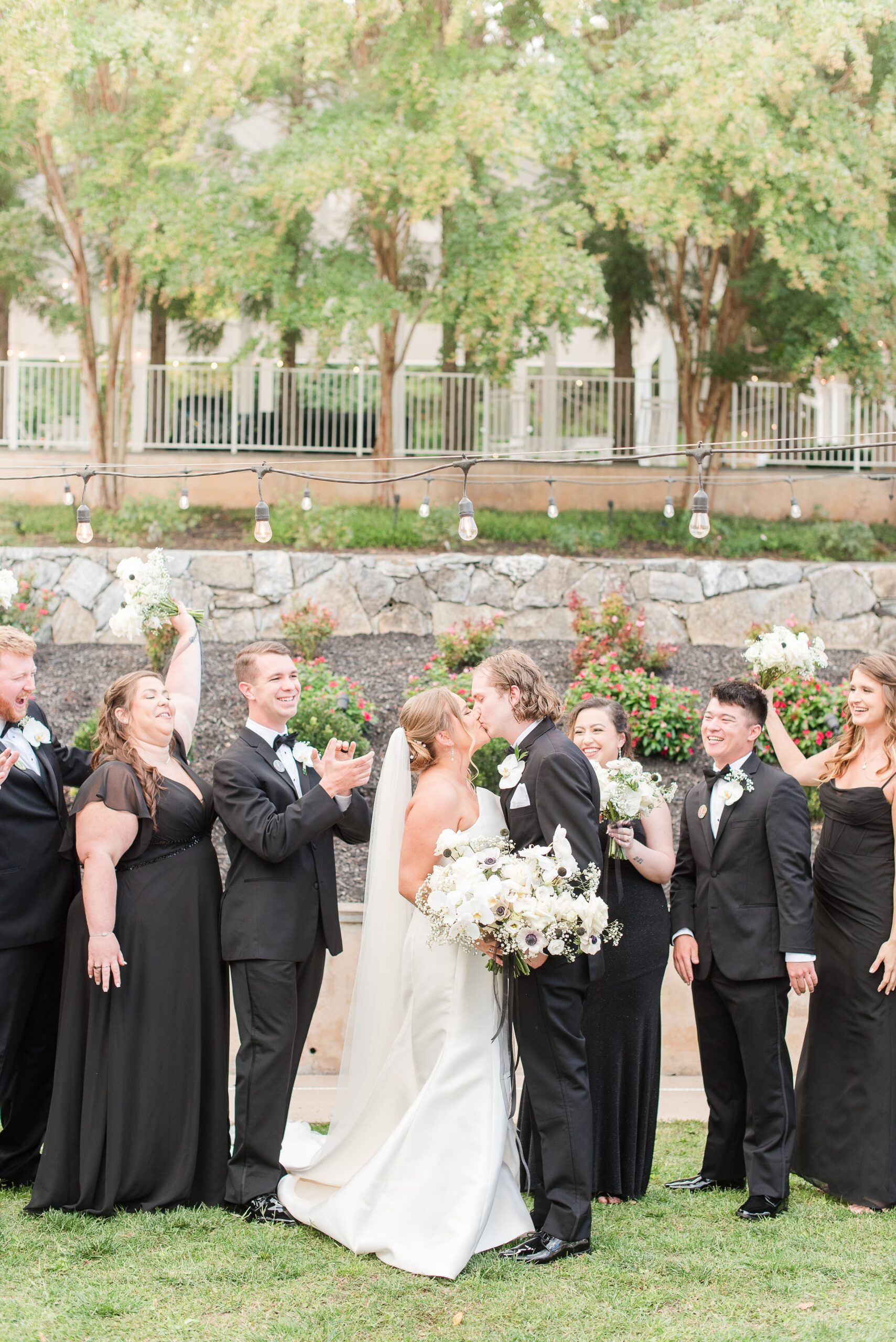 Newlyweds kiss in a garden while their wedding party cheers at their Milton Ridge Wedding