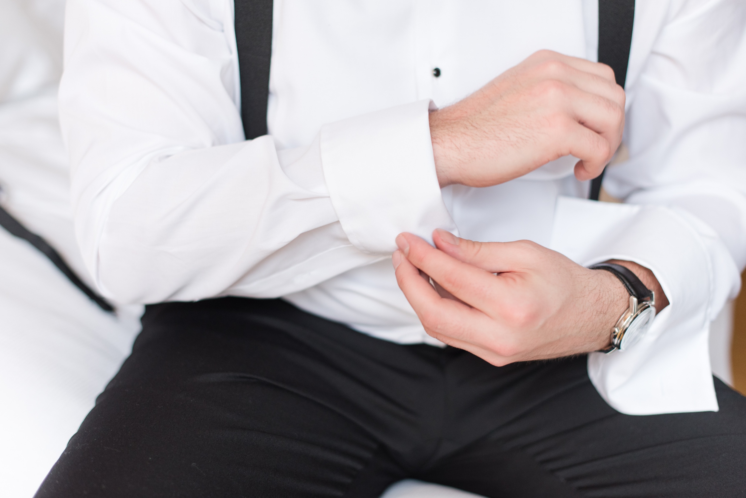 Details of a groom adjusting his cufflinks while sitting on a bed