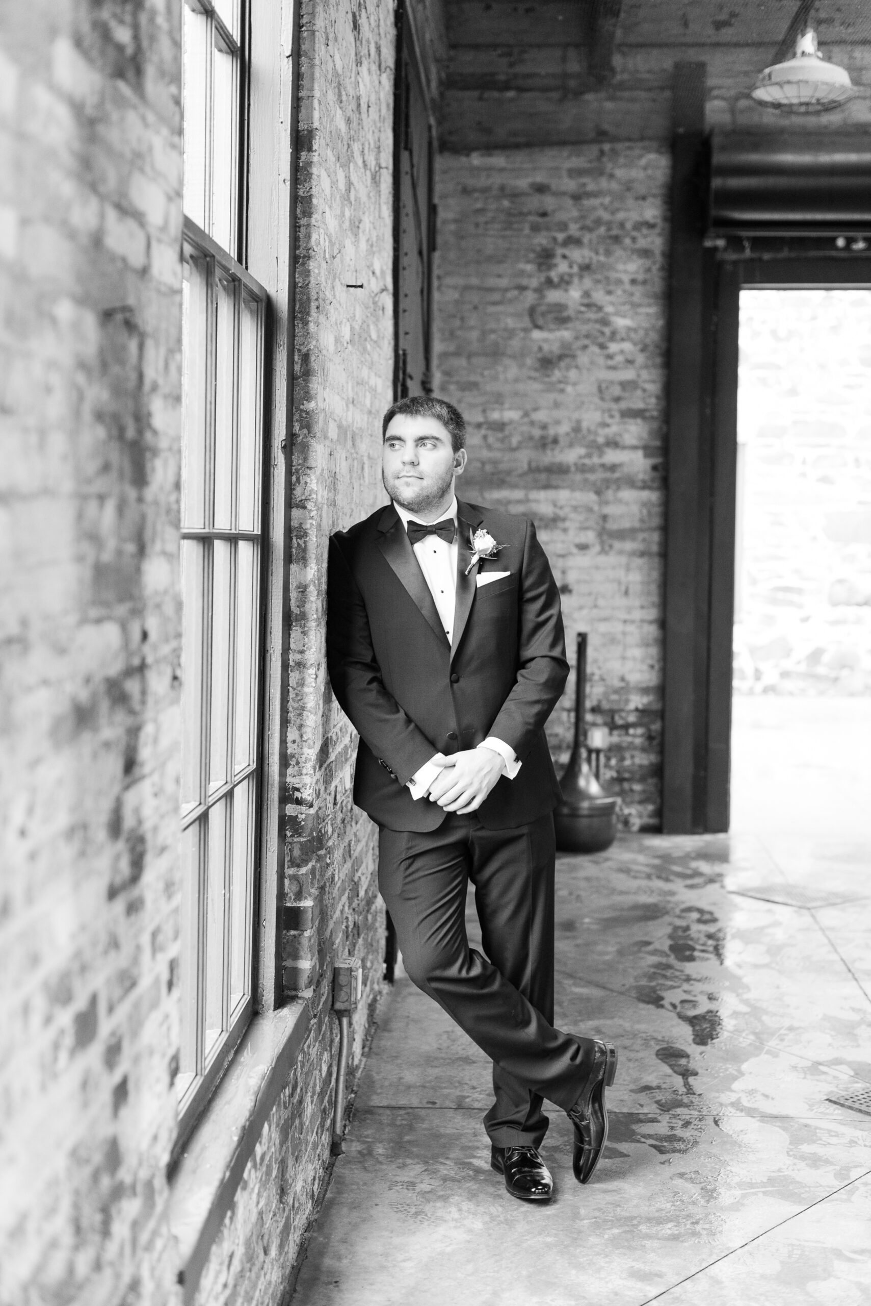 A groom leans on a wall while smiling out the window with hands crossed at his Mt. Washington Dye House Wedding