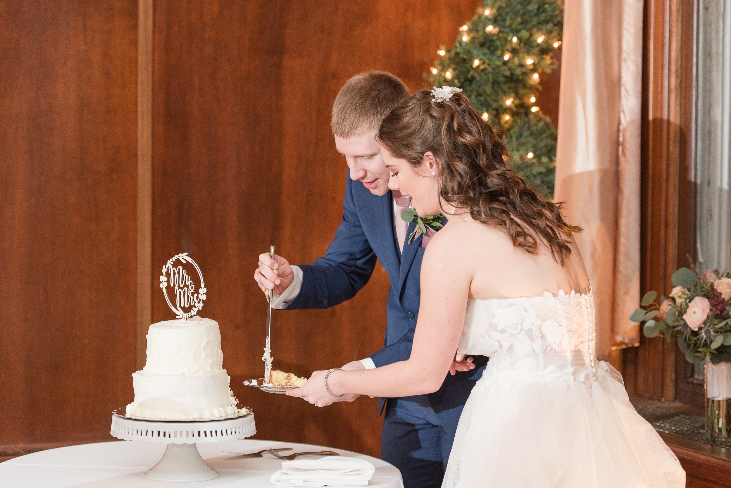 Newlyweds happily cut their white two tier cake on a white stand and white linen