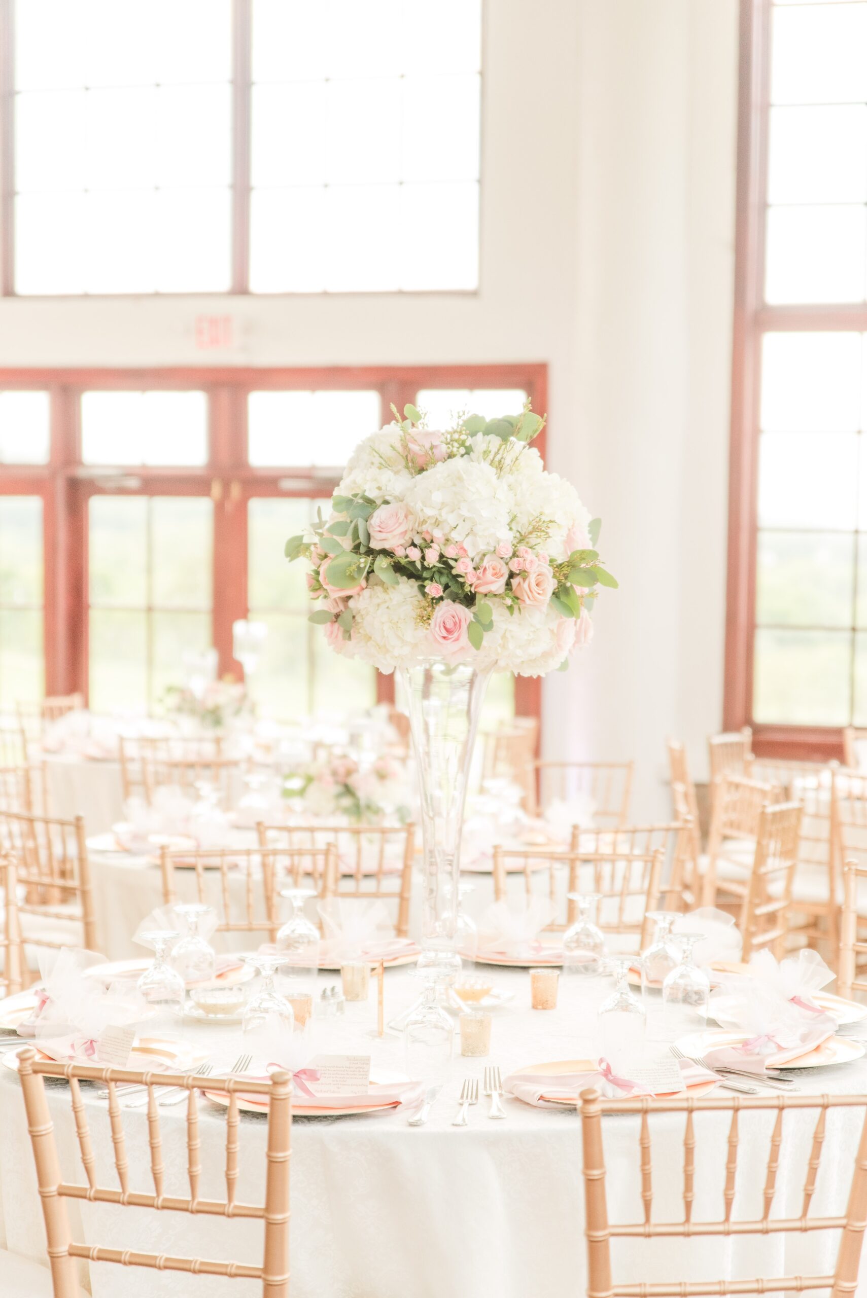 Details of a Raspberry Plain Manor Wedding reception table set up with tall white and pink centerpiece and wooden chairs