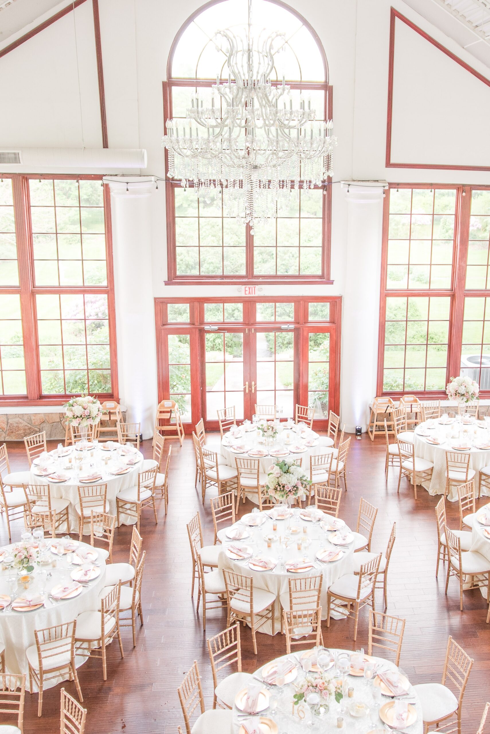 A view down on a Raspberry Plain Manor Wedding reception with wooden chairs and white linens under a large chandelier