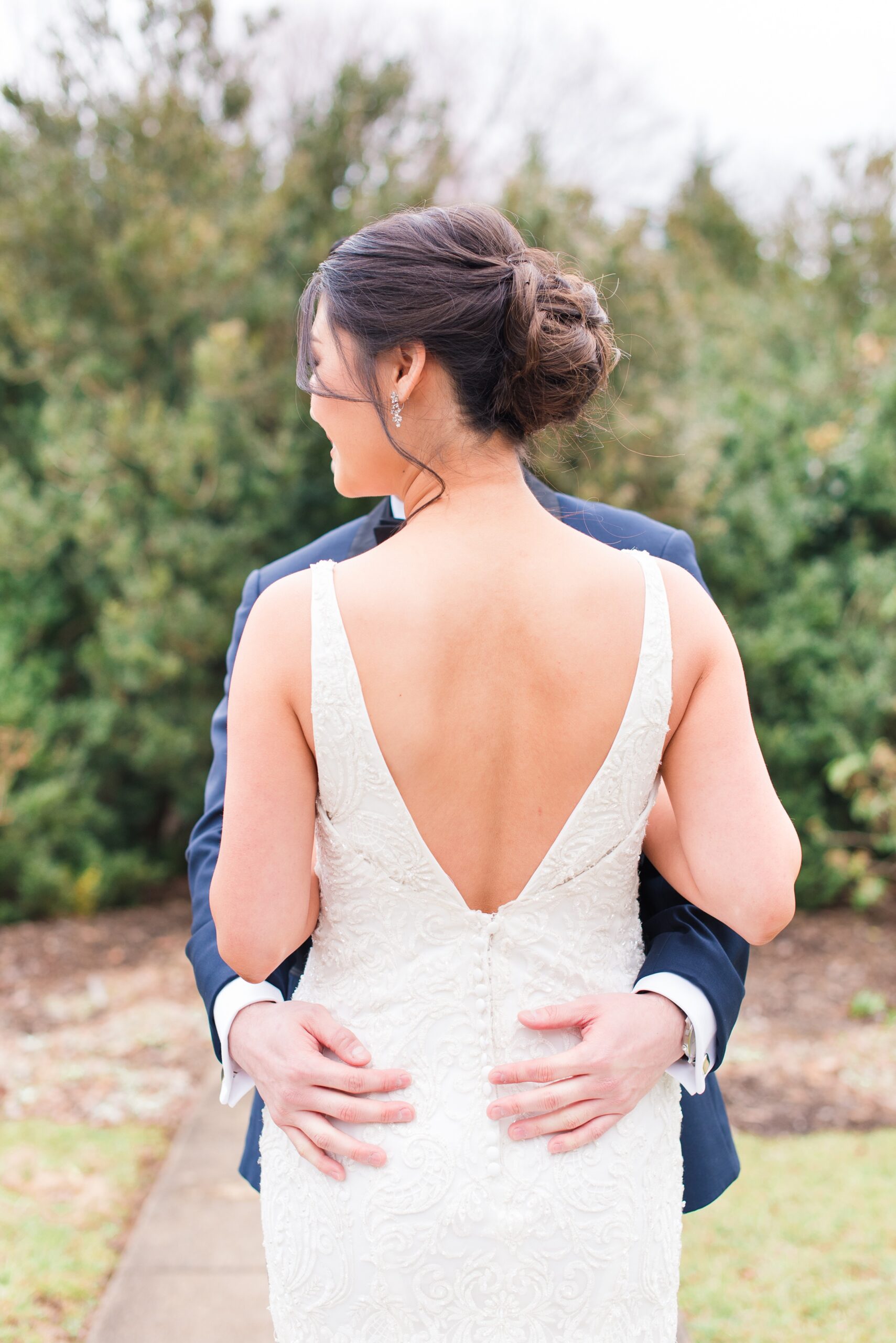 Newlyweds stand close on a sidewalk smiling over their shoulders at their Raspberry Plain Manor Wedding