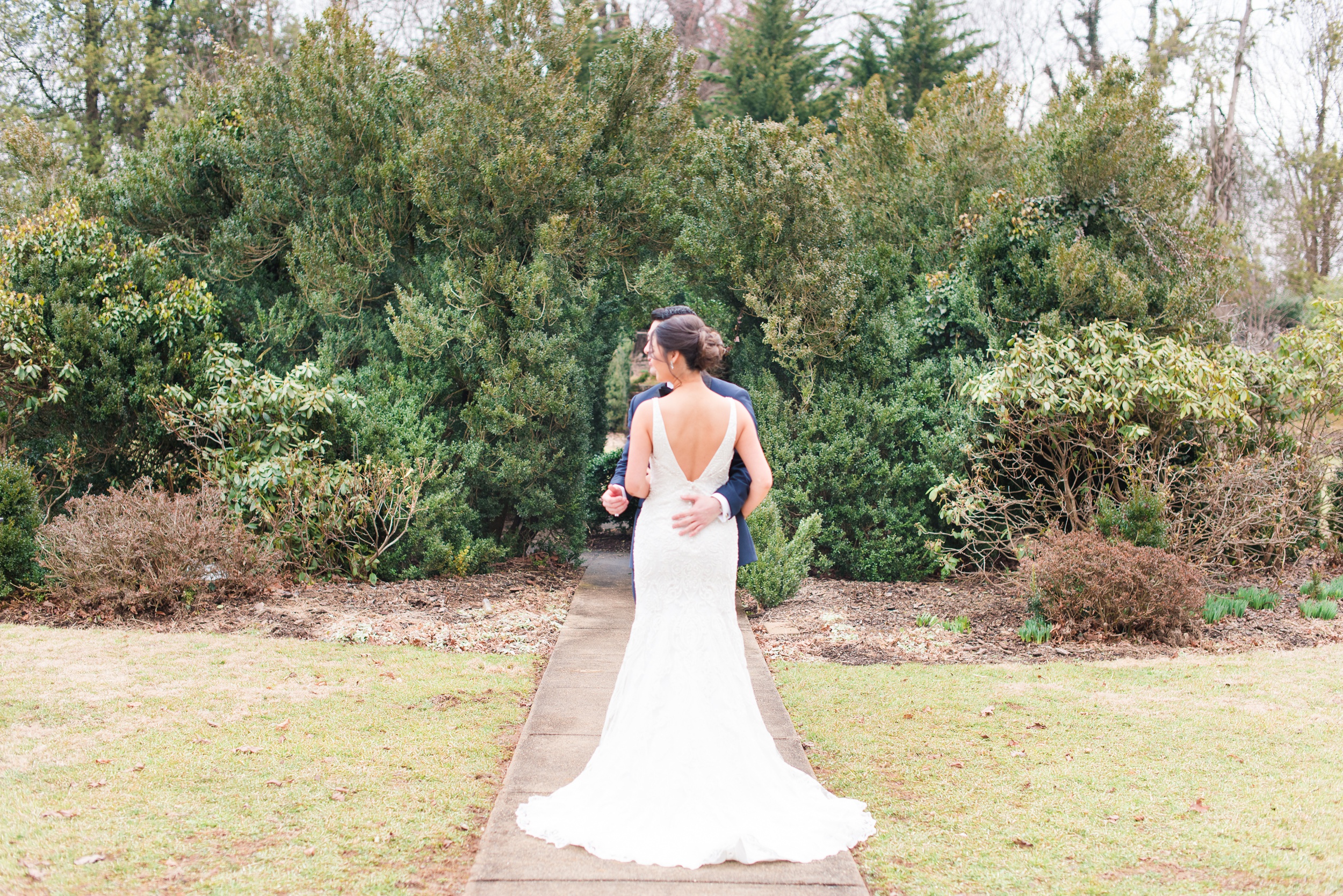 Newlyweds hug and look over their shoulder while exploring a garden sidewalk at their Raspberry Plain Manor Wedding