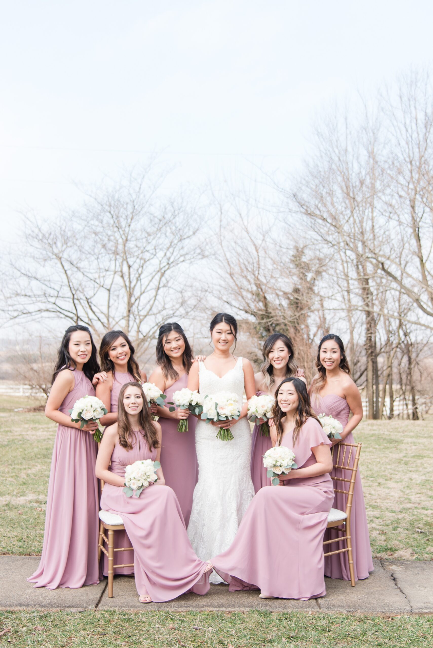 A bride stands with her bridesmaids in a sidewalk in fall holding white rose bouquets