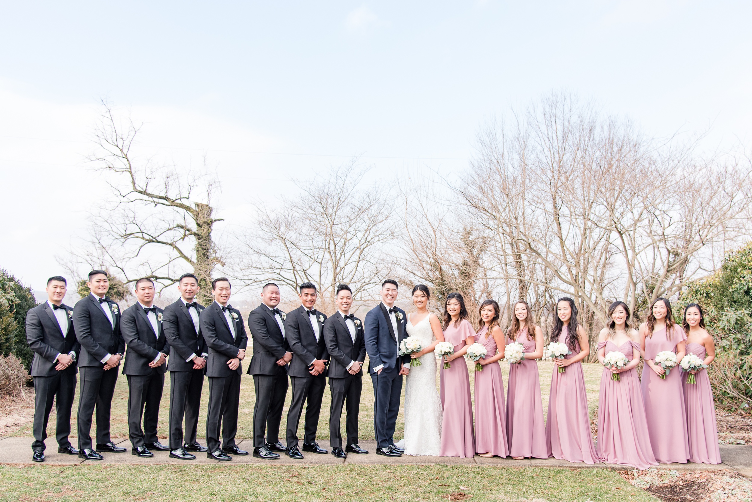 Newlyweds stand in a sidewalk in fall with their large wedding party on either side