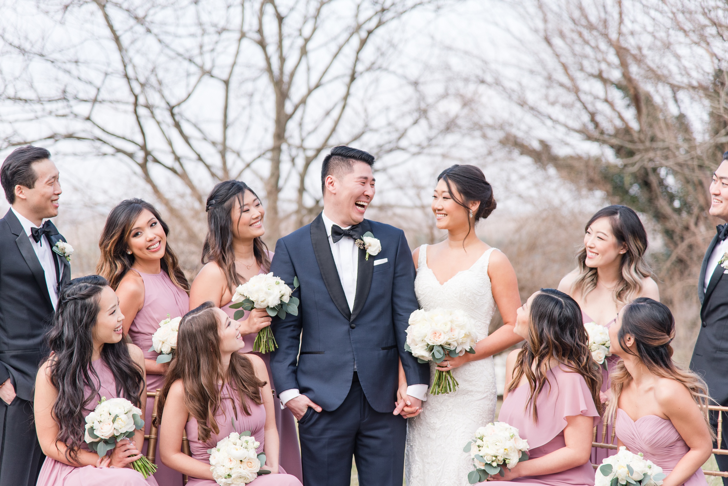 Newlyweds laugh while standing with their wedding party holding hands