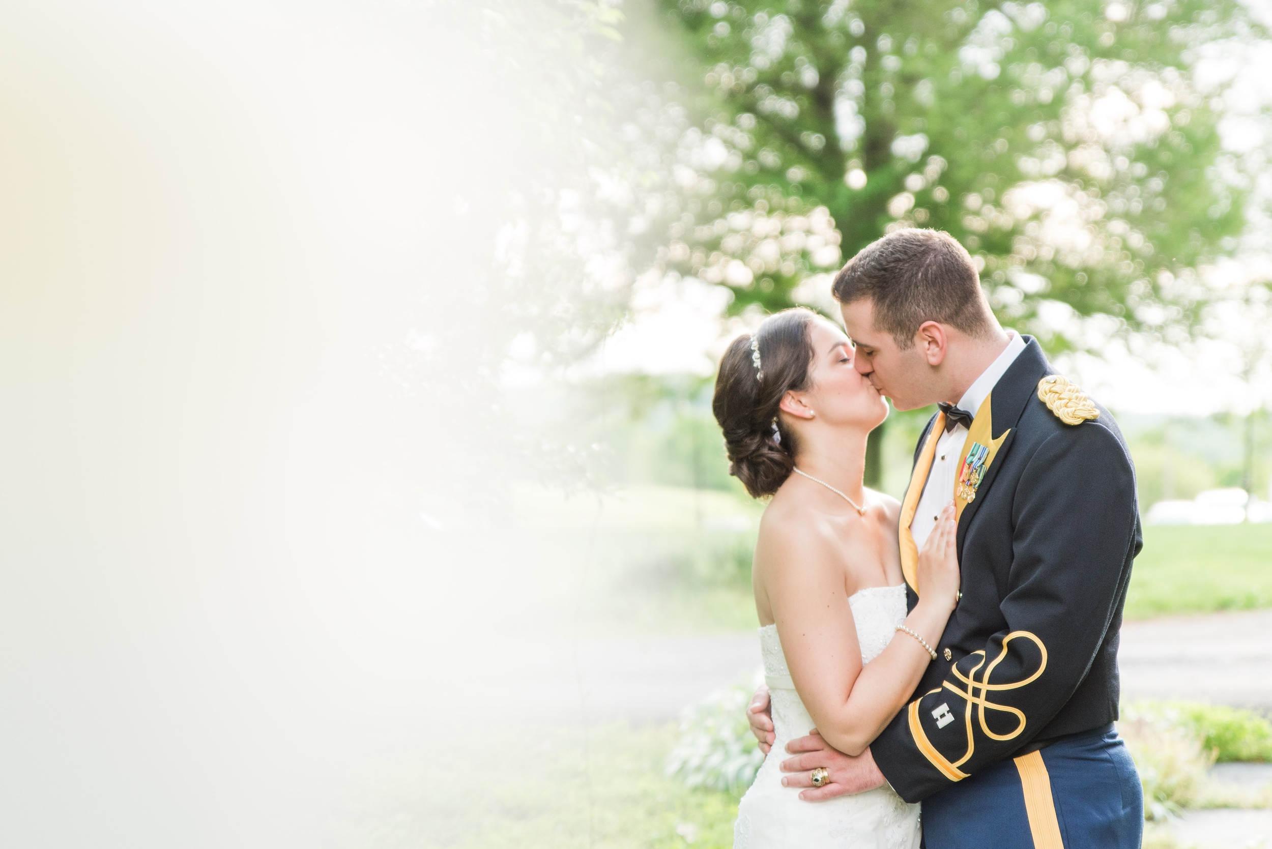 Newlyweds kiss while standing in a garden in a military uniform and lace dress