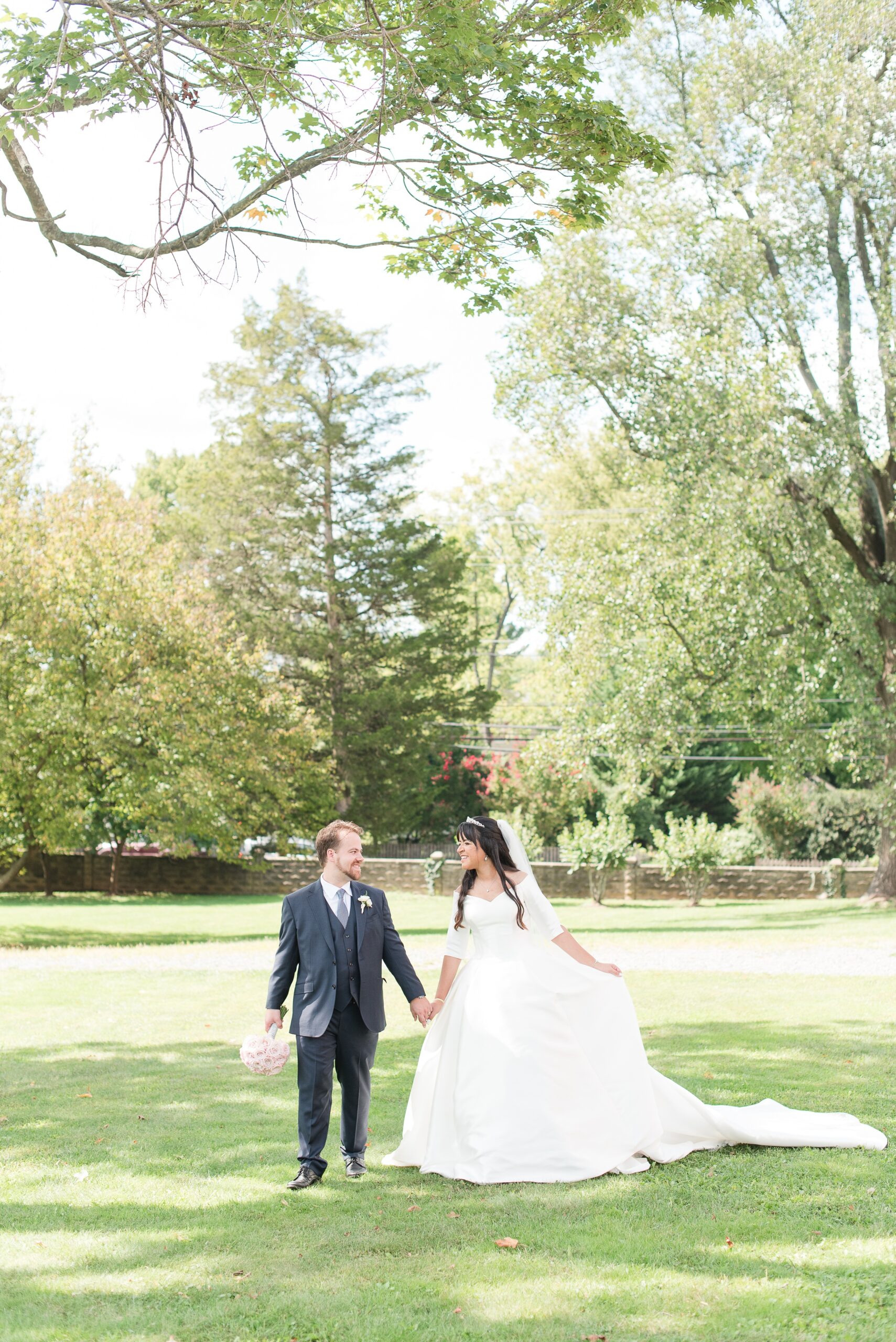 Newlyweds walk through a lawn holding hands and smiling at each other at their River Creek Club Wedding