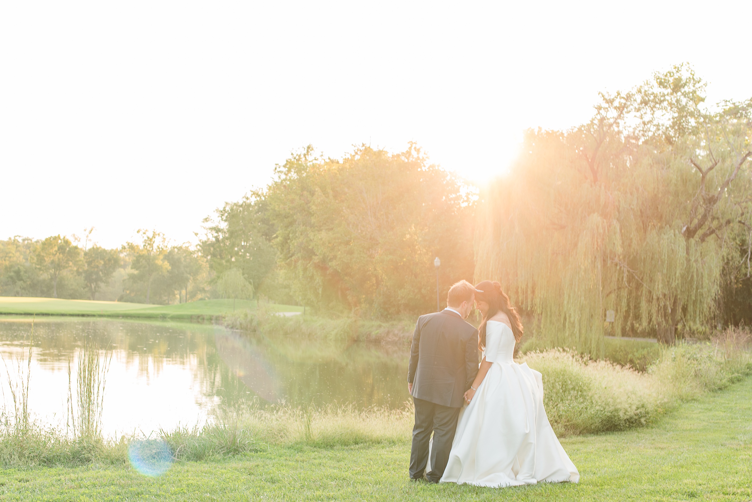 Newlyweds touch foreheads and hold hands while watching the sunset over the pond at the River Creek Club Wedding venue
