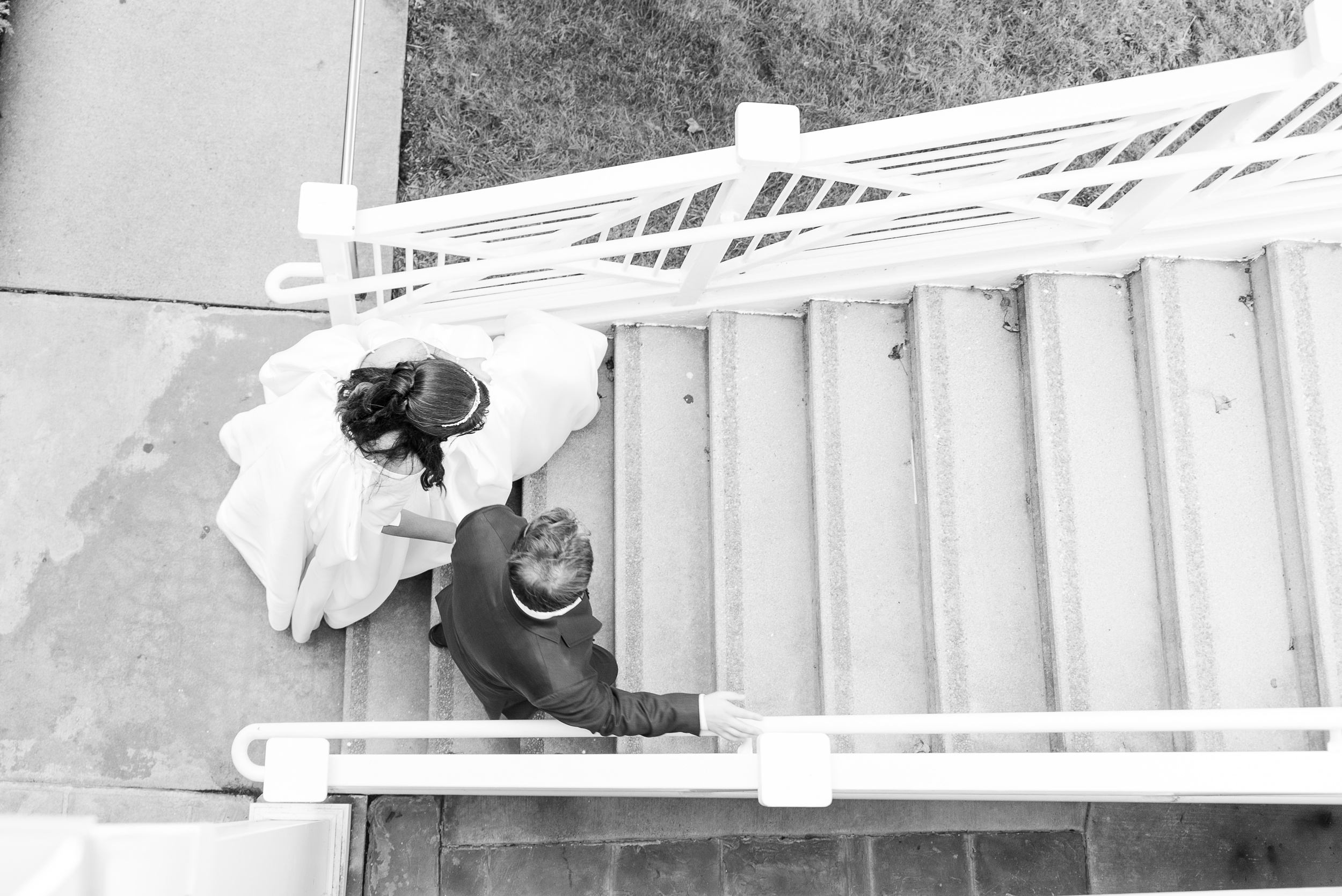 A groom helps his bride up a set of stairs during their River Creek Club Wedding