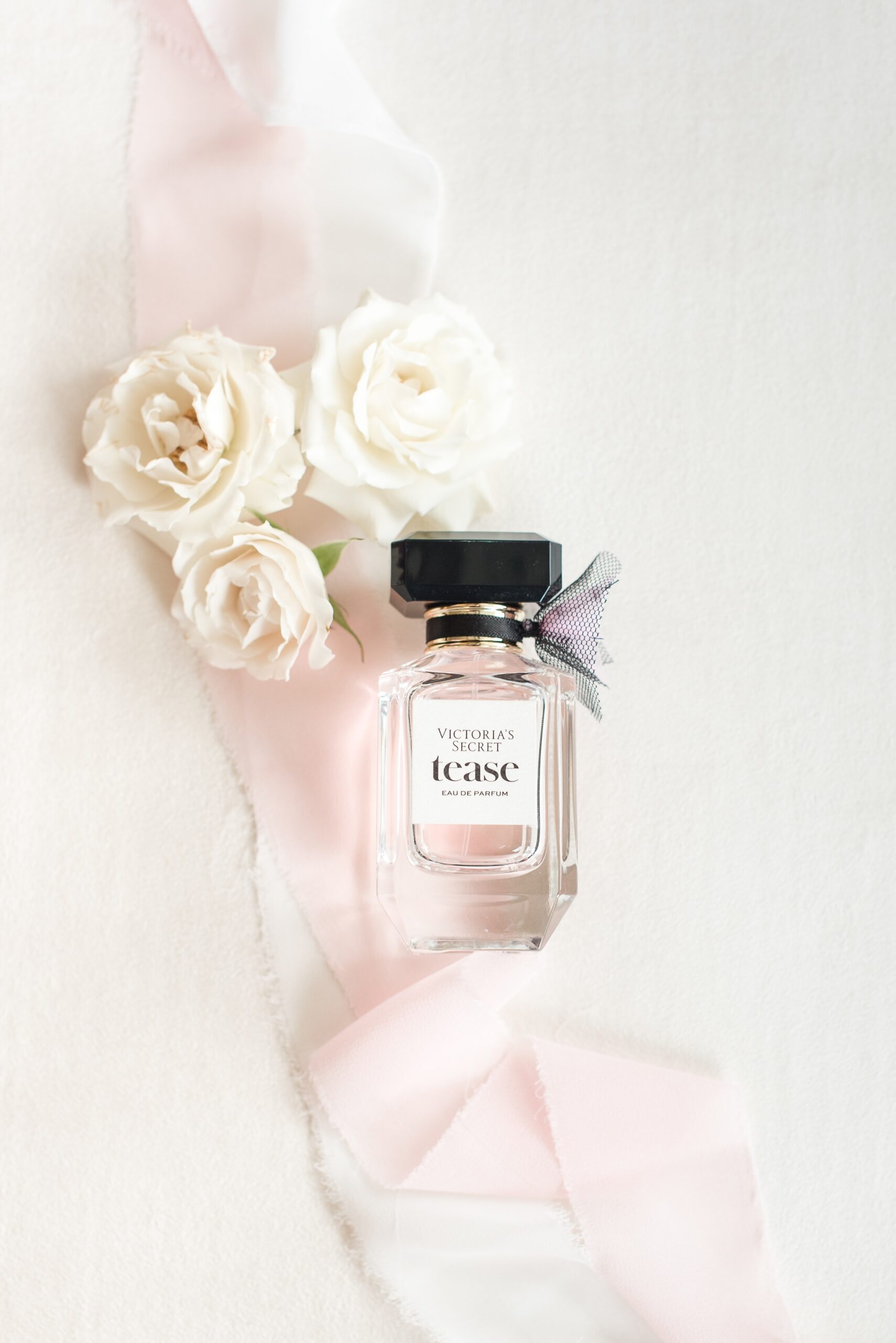 Details of a perfume on a table with white roses