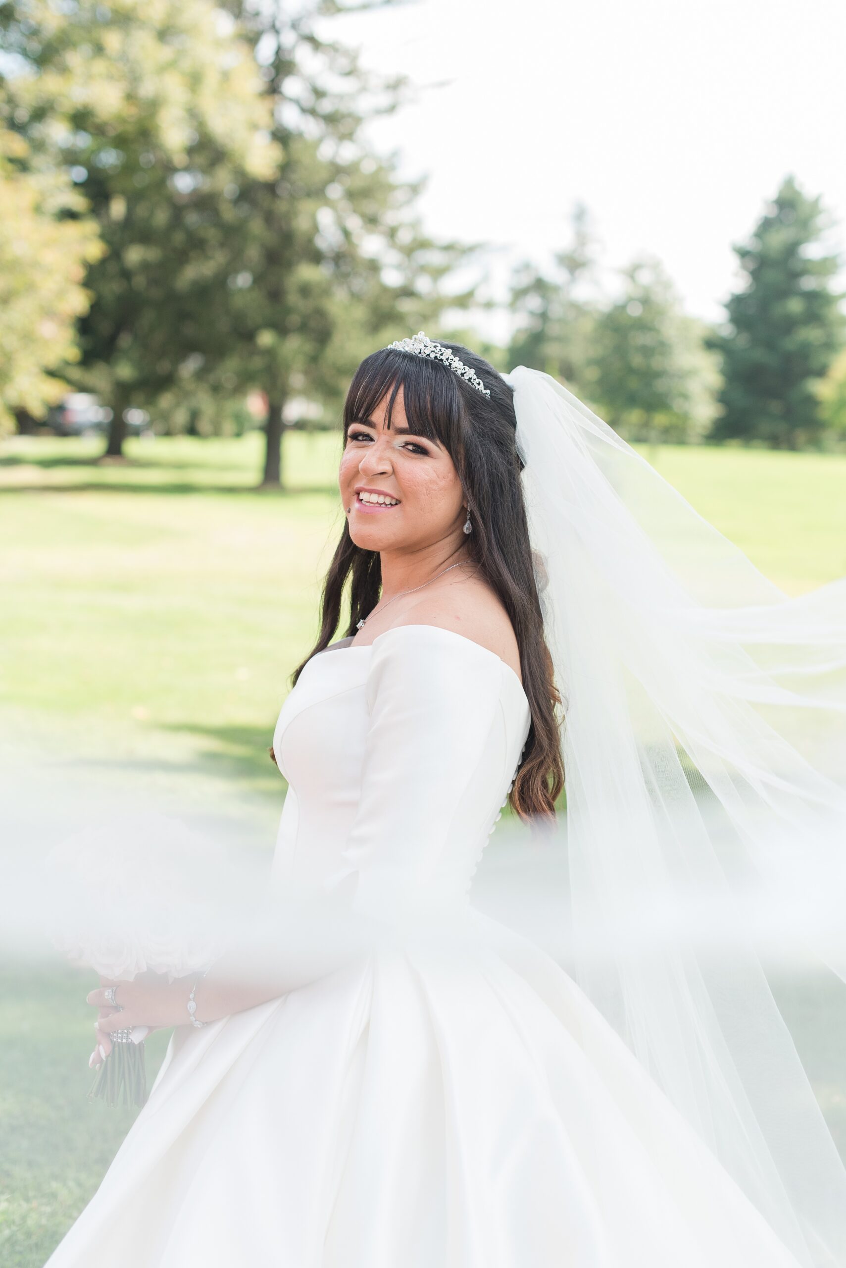 A bride smiles while her veil blows in the wind around her in a lawn