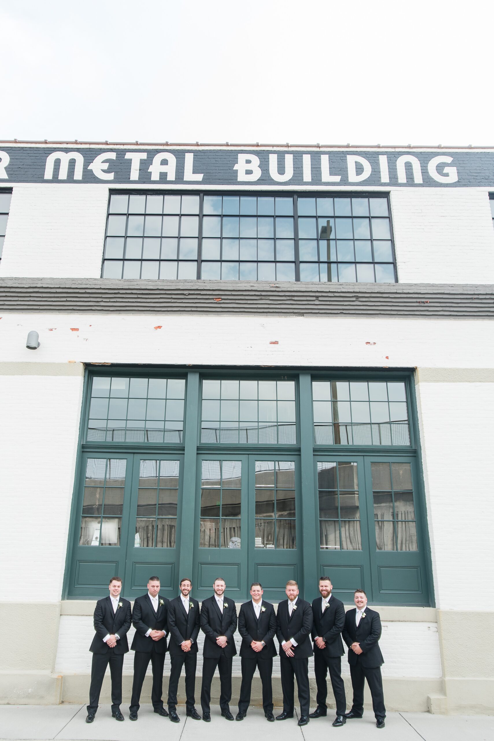 A groom and his wedding party stand under the sign at The Winslow Baltimore with hands crossed in black suits