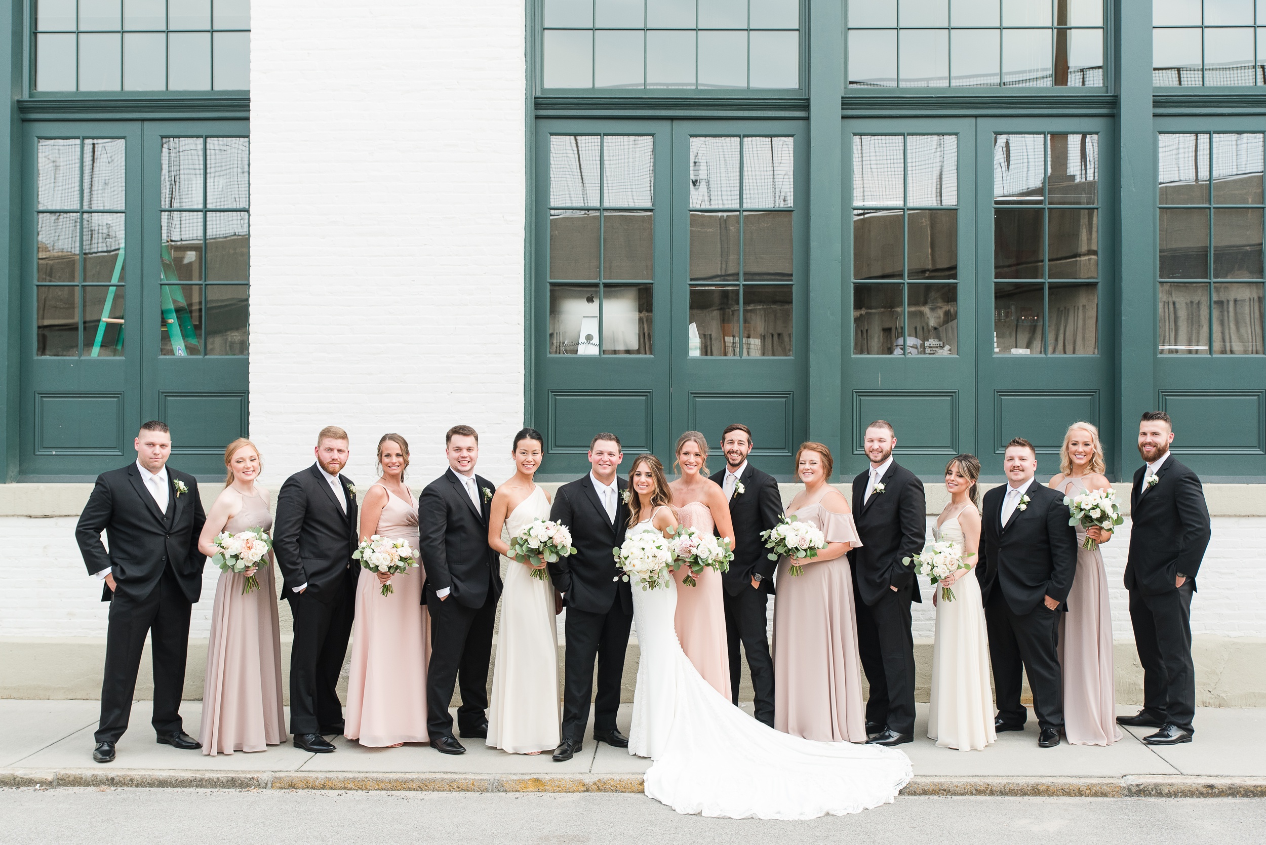 Newlyweds stand on a sidewalk with their large wedding party outside The Winslow Baltimore