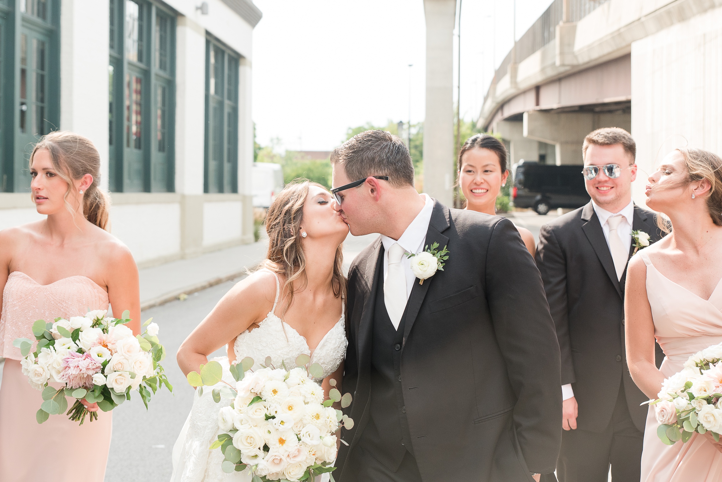 Newlyweds kiss while walking in an alley with their wedding party