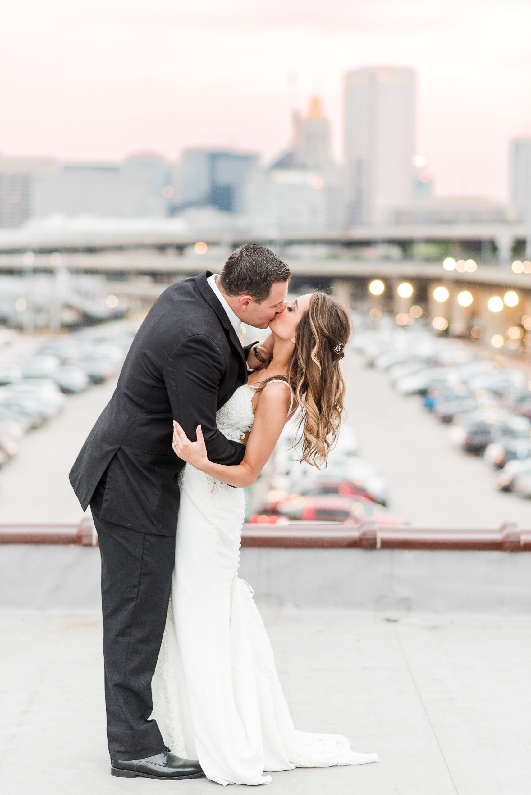 Newlyweds kiss and dip while standing on a rooftop at sunset