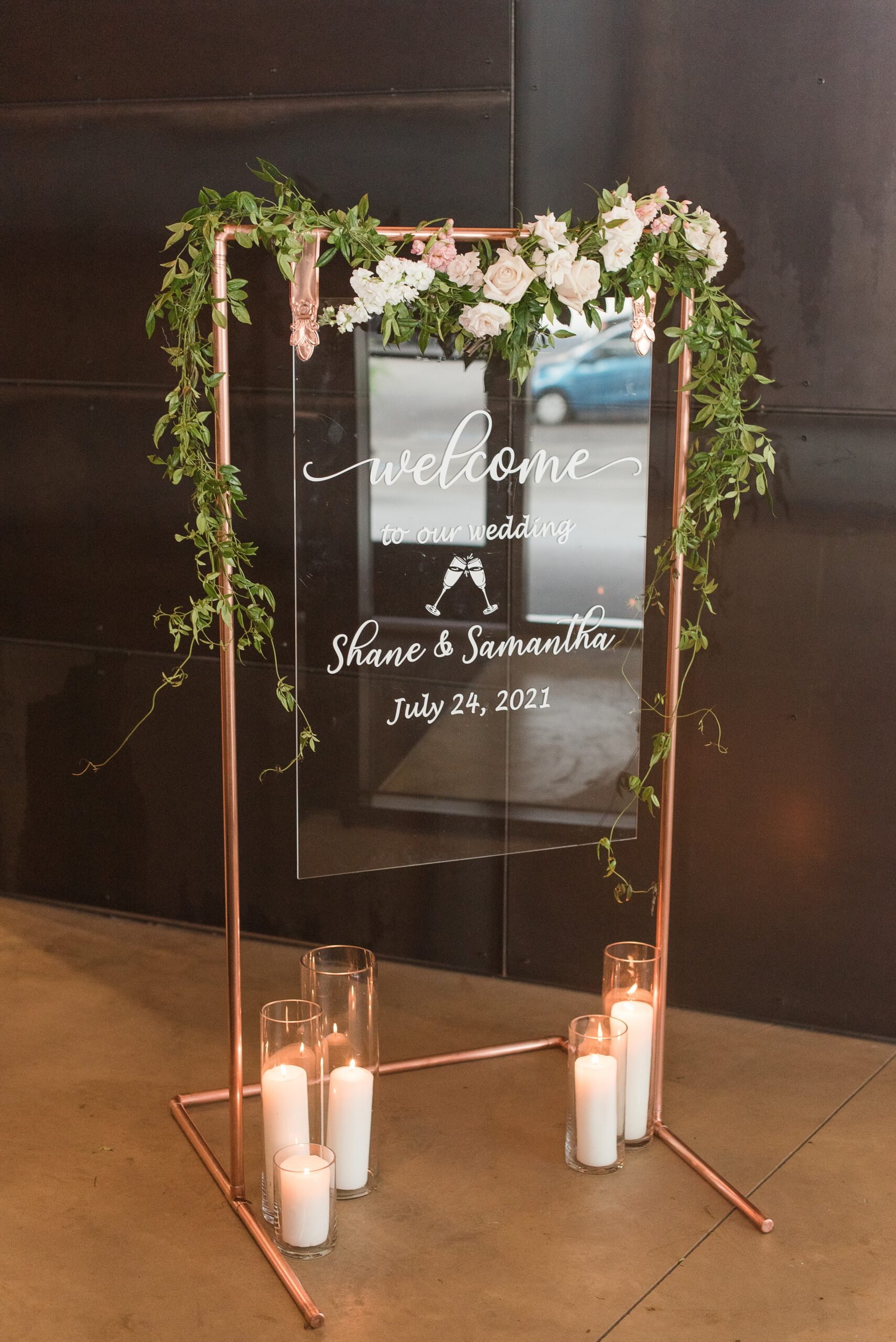 Details of a glass welcome sign for a wedding with candles and florals