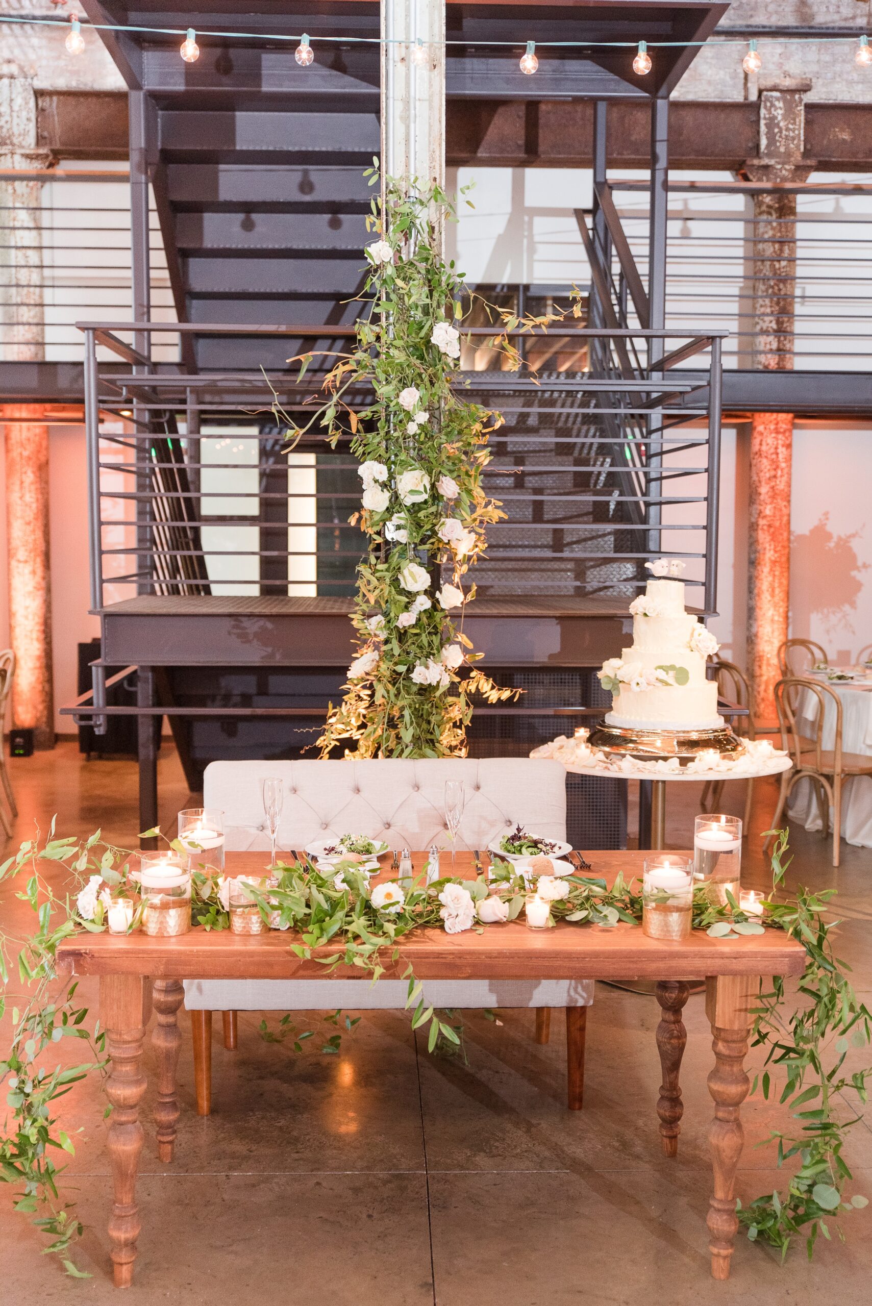 Details of a wedding head table made of wood with lush greenery and candles at The Winslow Baltimore