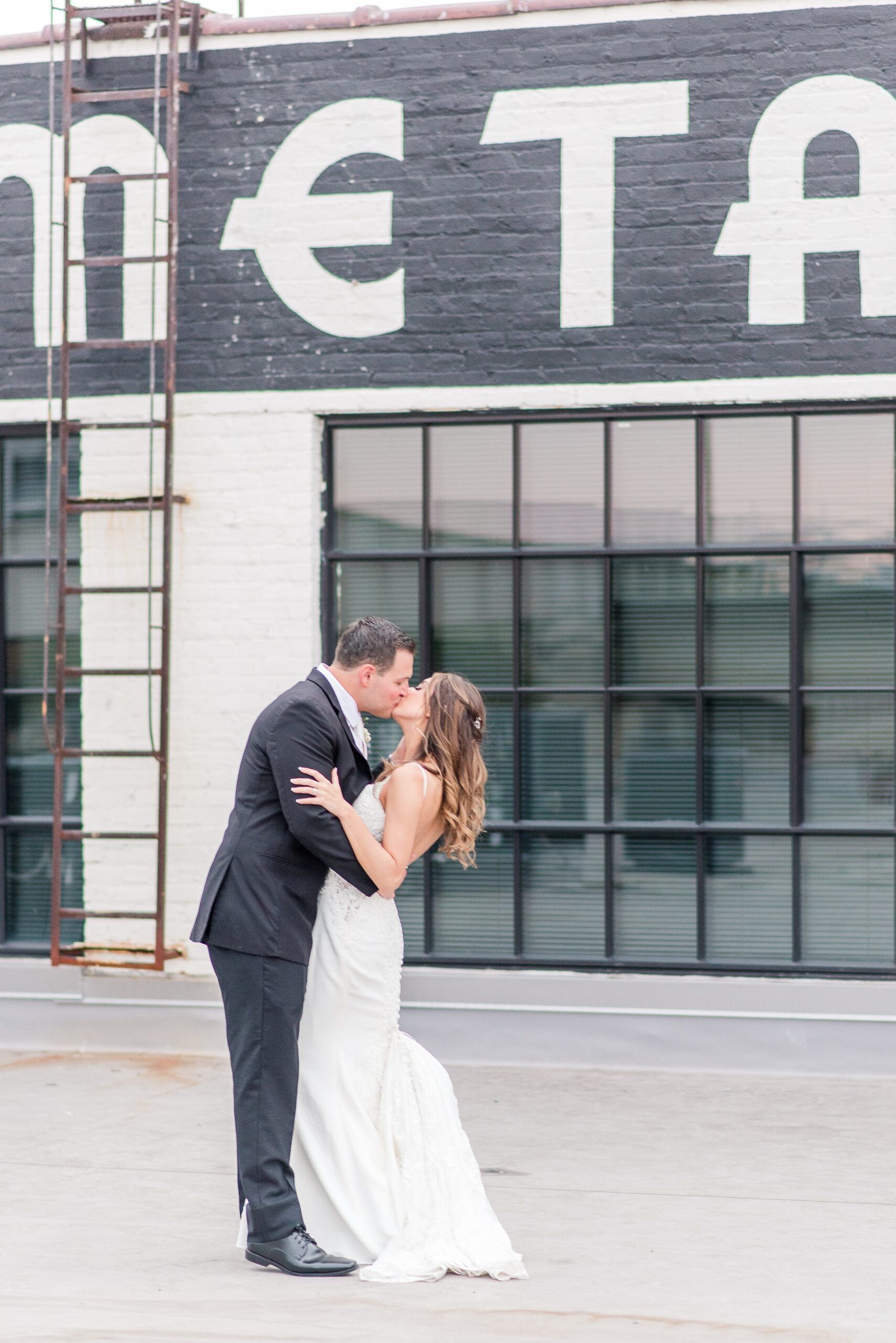 Newlyweds kiss while standing on an industrial rooftop