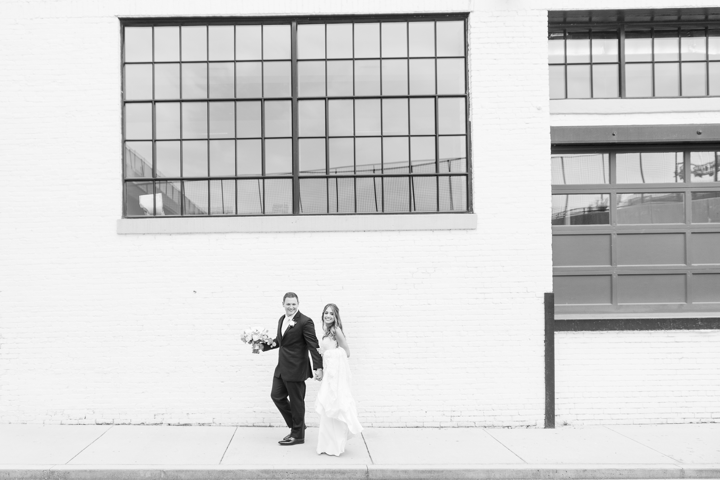 A black and white image of newlyweds walking through an alley and holding hands