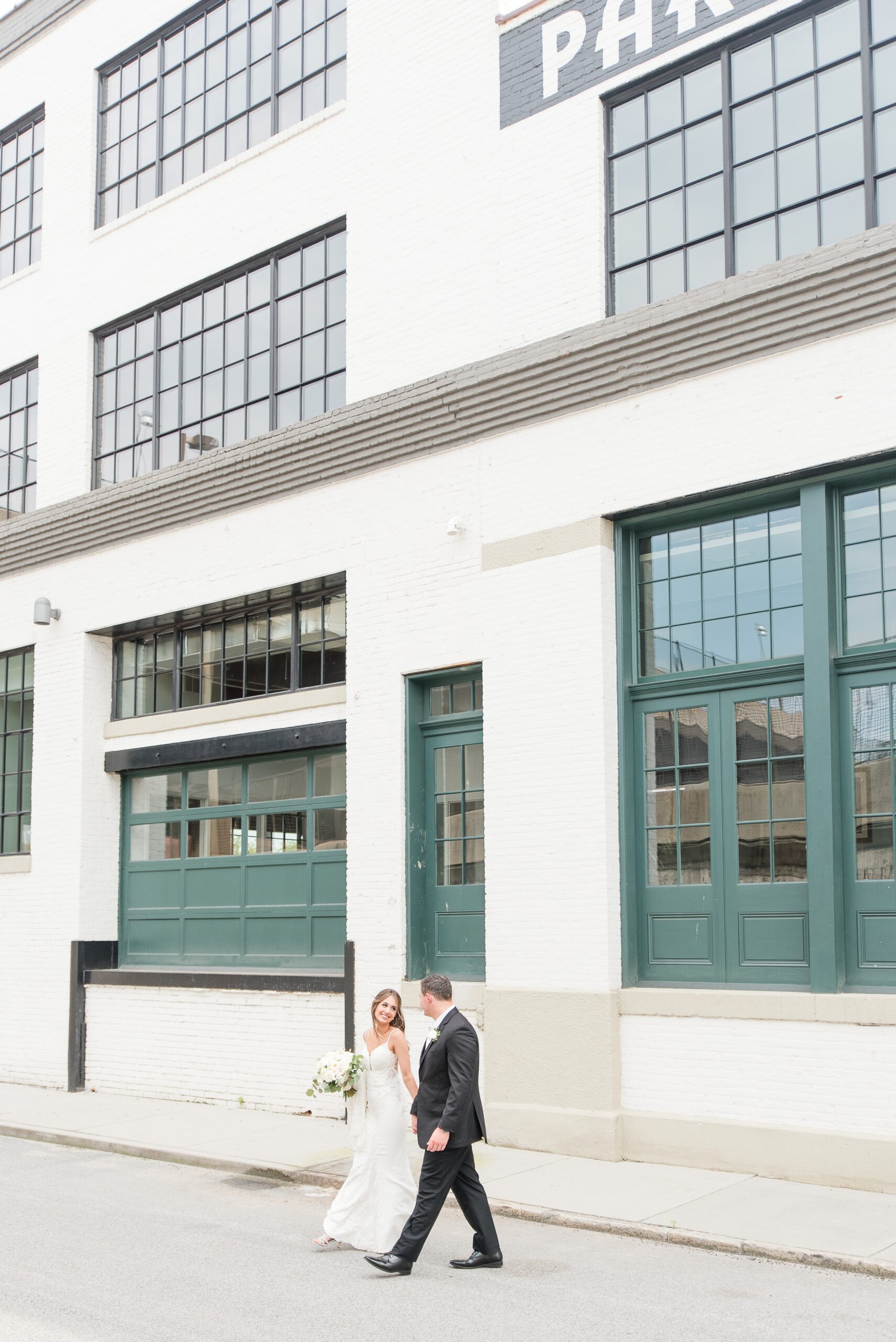 Newlyweds walk through an alley holding hands and smiling at each other at The Winslow Baltimore