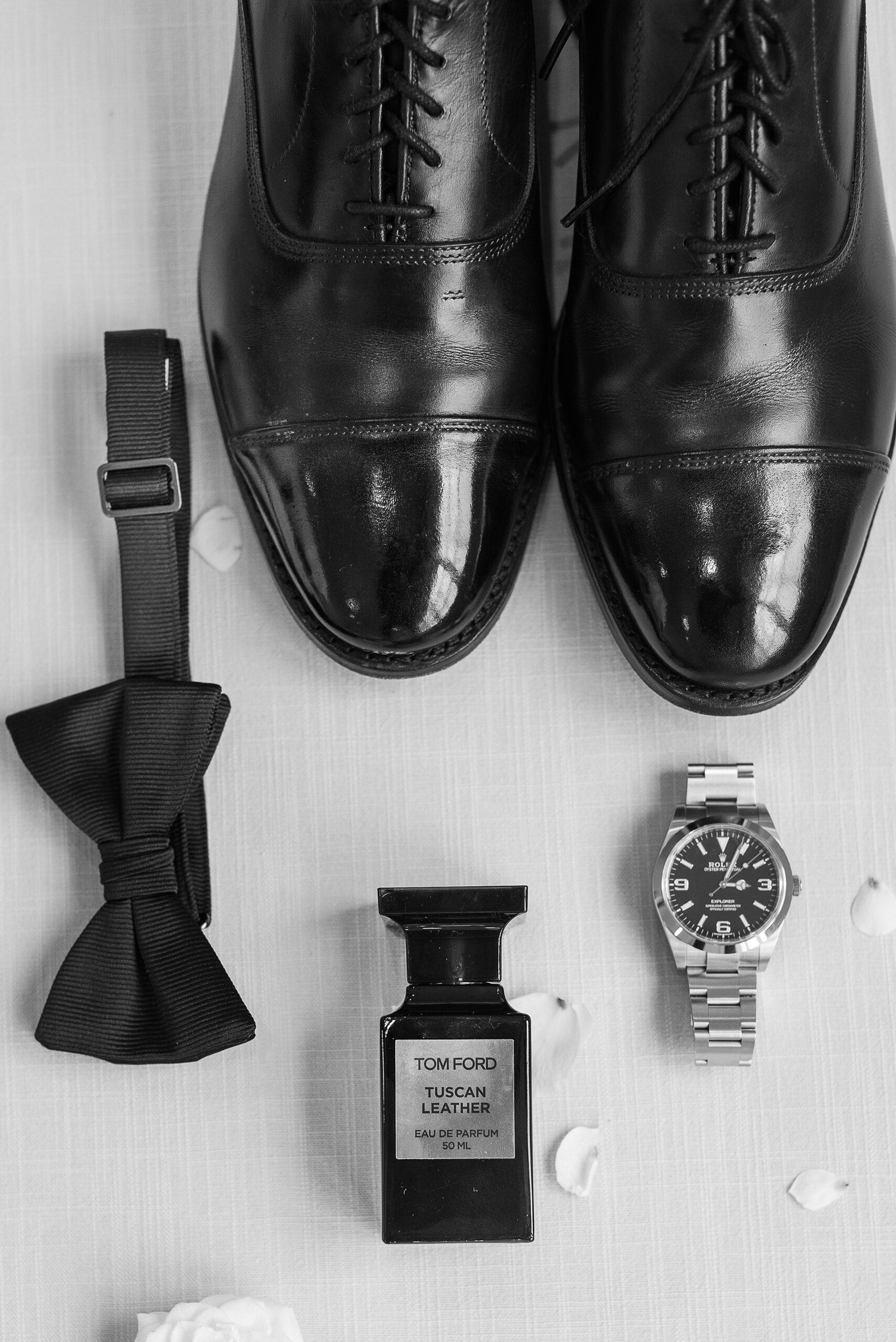 Details of a groom's shoes, bowtie, watch and cologne on a table