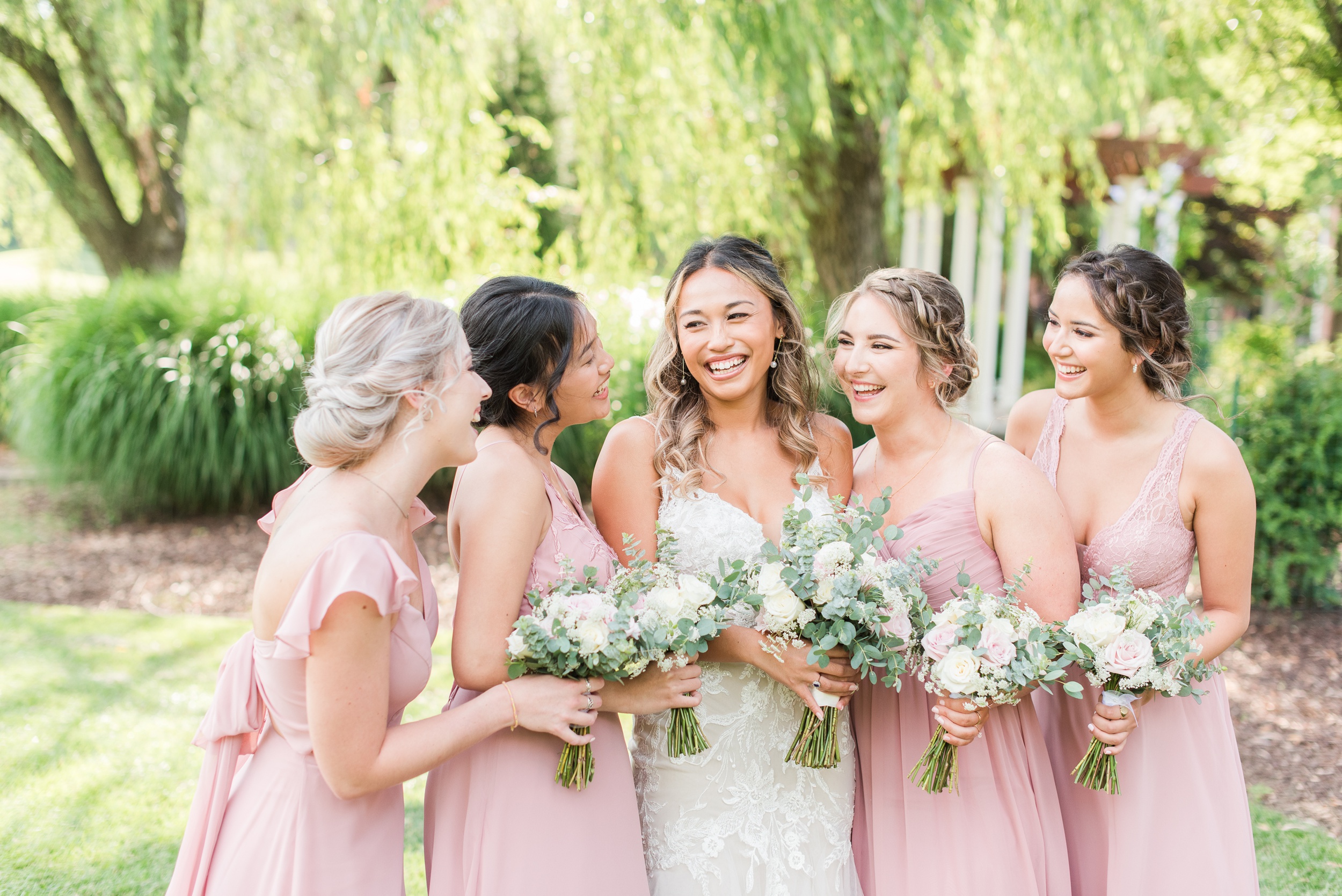 A bride laughs while standing in a garden with her bridesmaids in pink dresses