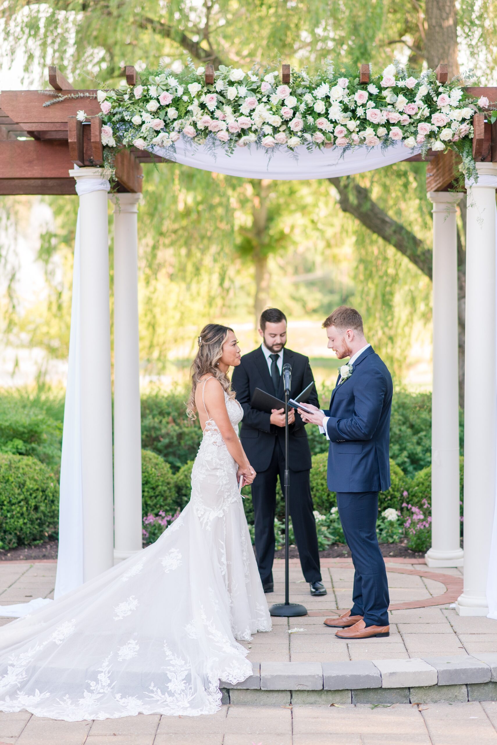 A groom reads his vows to his bride under a beautiful wedding pergola on a stone patio