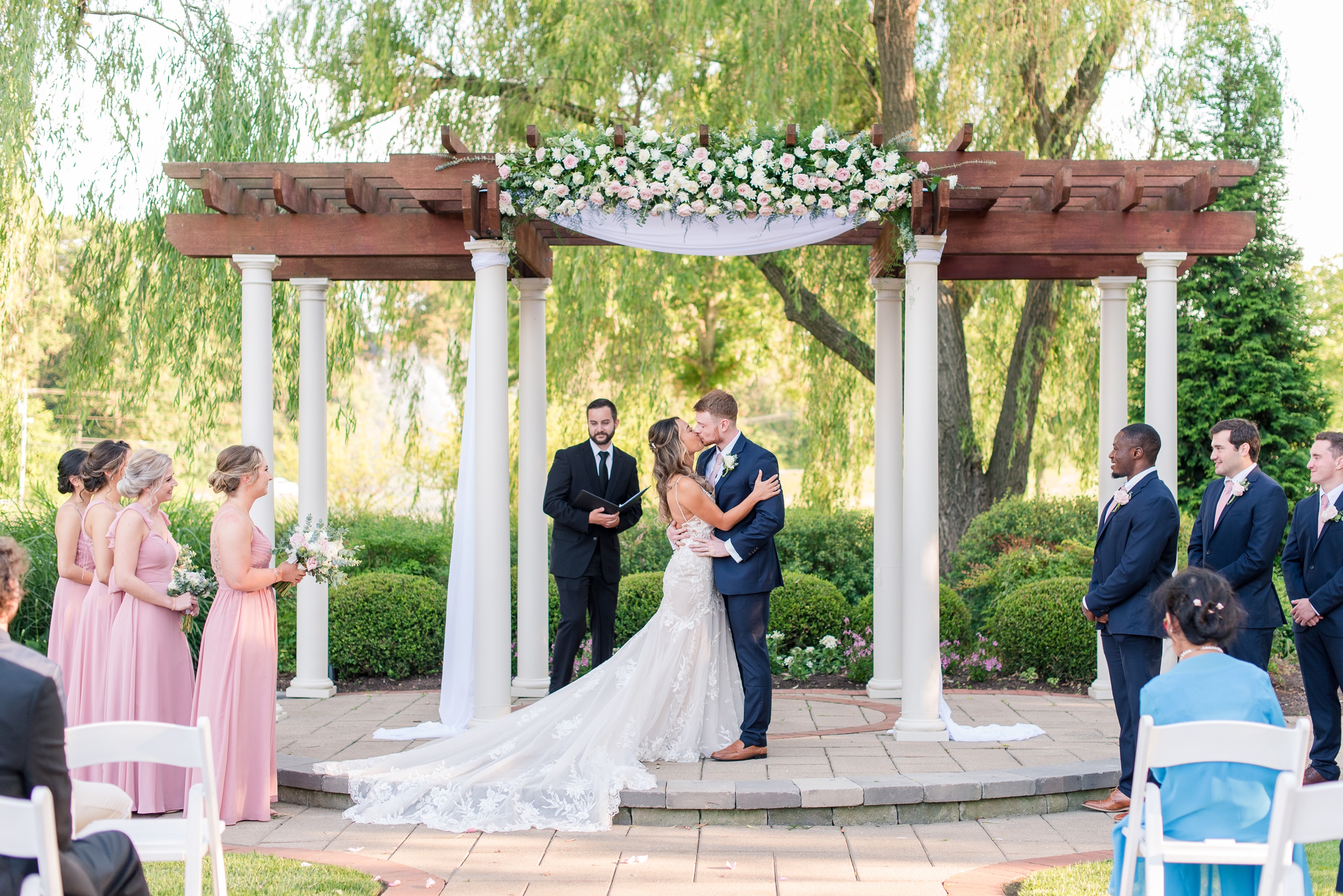 Newlyweds kiss under a decorated pergola to end their wedding ceremony