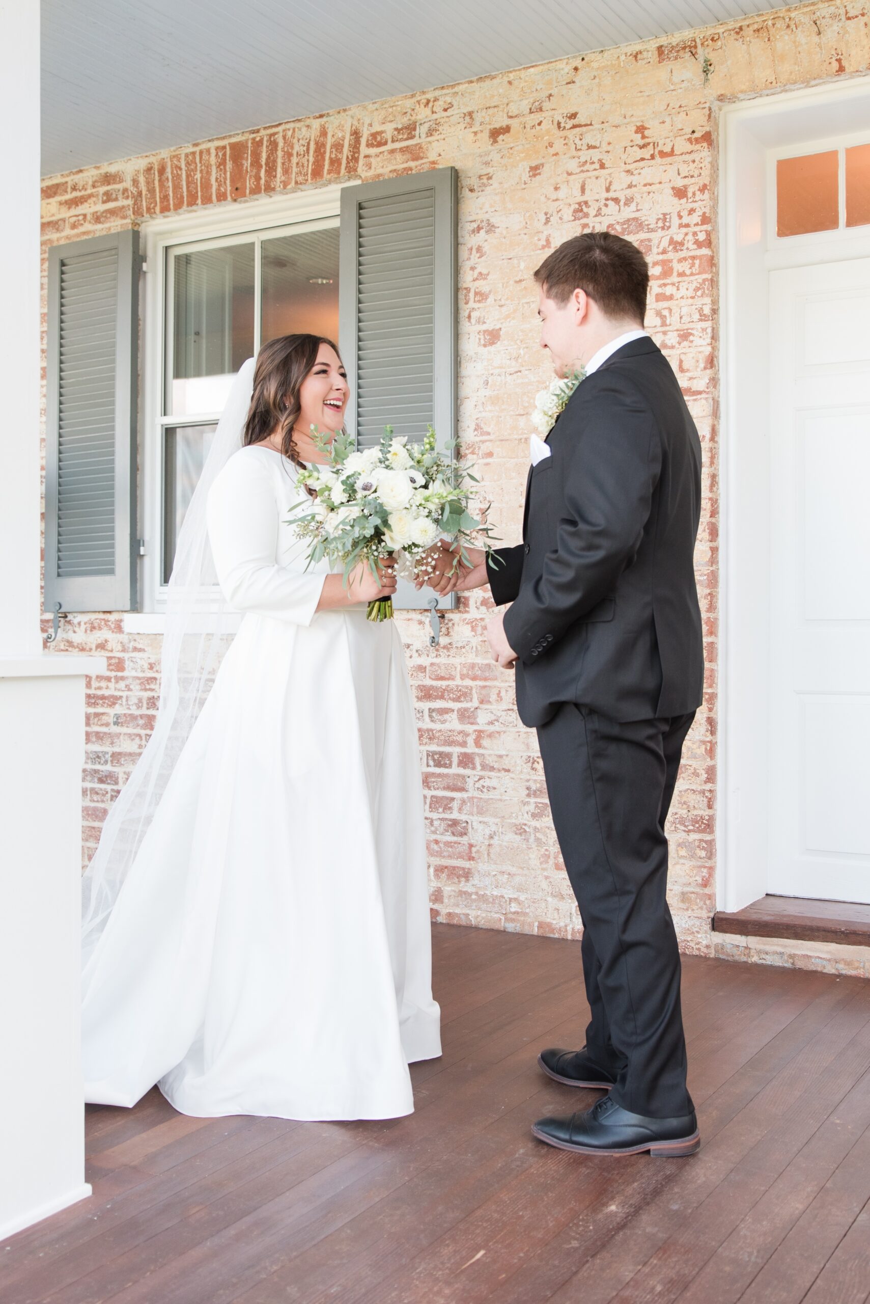 A bride and groom happily share a first look moment on the front porch
