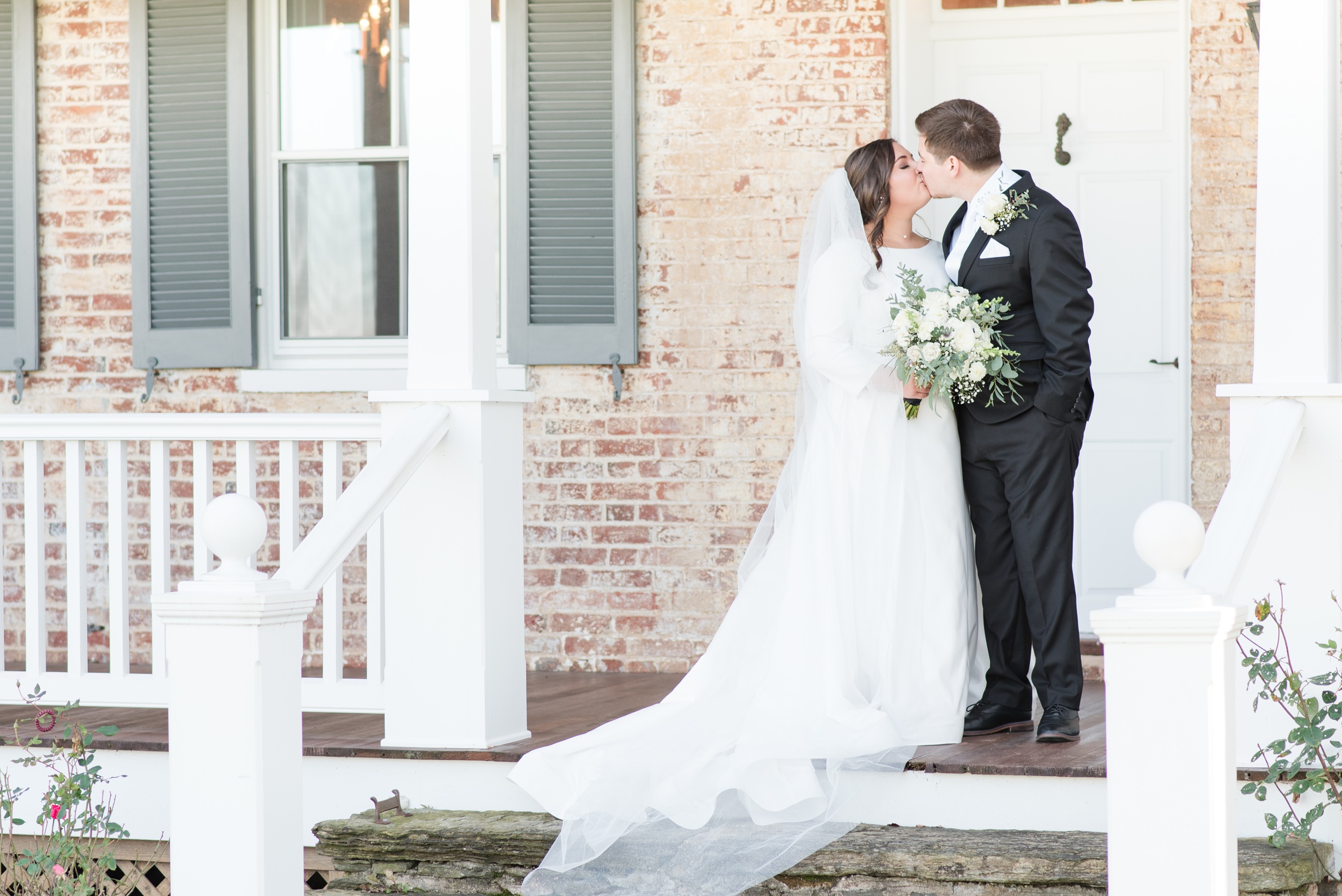 A bride and groom kiss while standing on the front porch steps of the Walkers Overlook Wedding venue