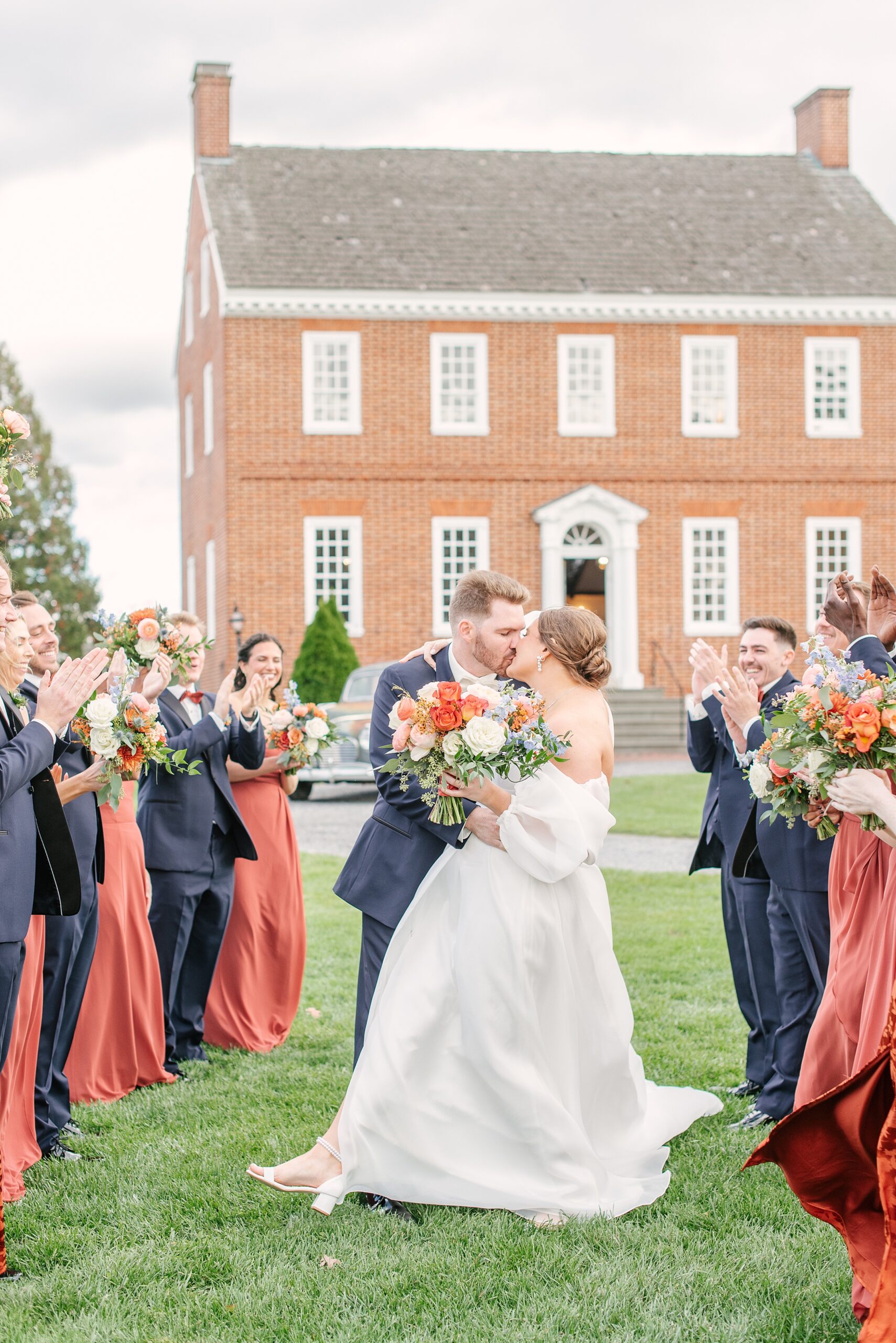 Newlyweds kiss to applause and cheers from their wedding party that surrounds them