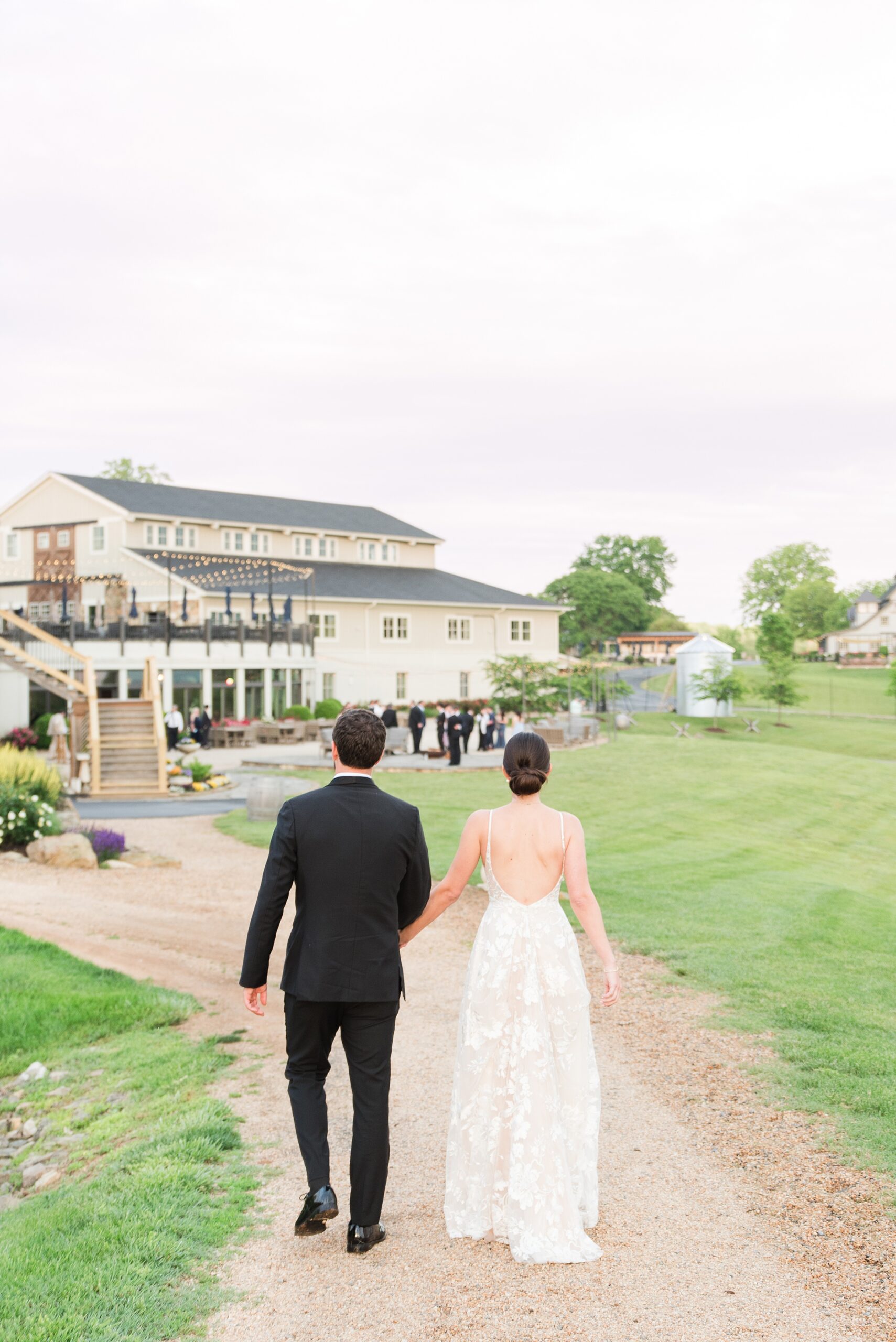 Newlyweds hold hands and walk down a gravel path to their reception