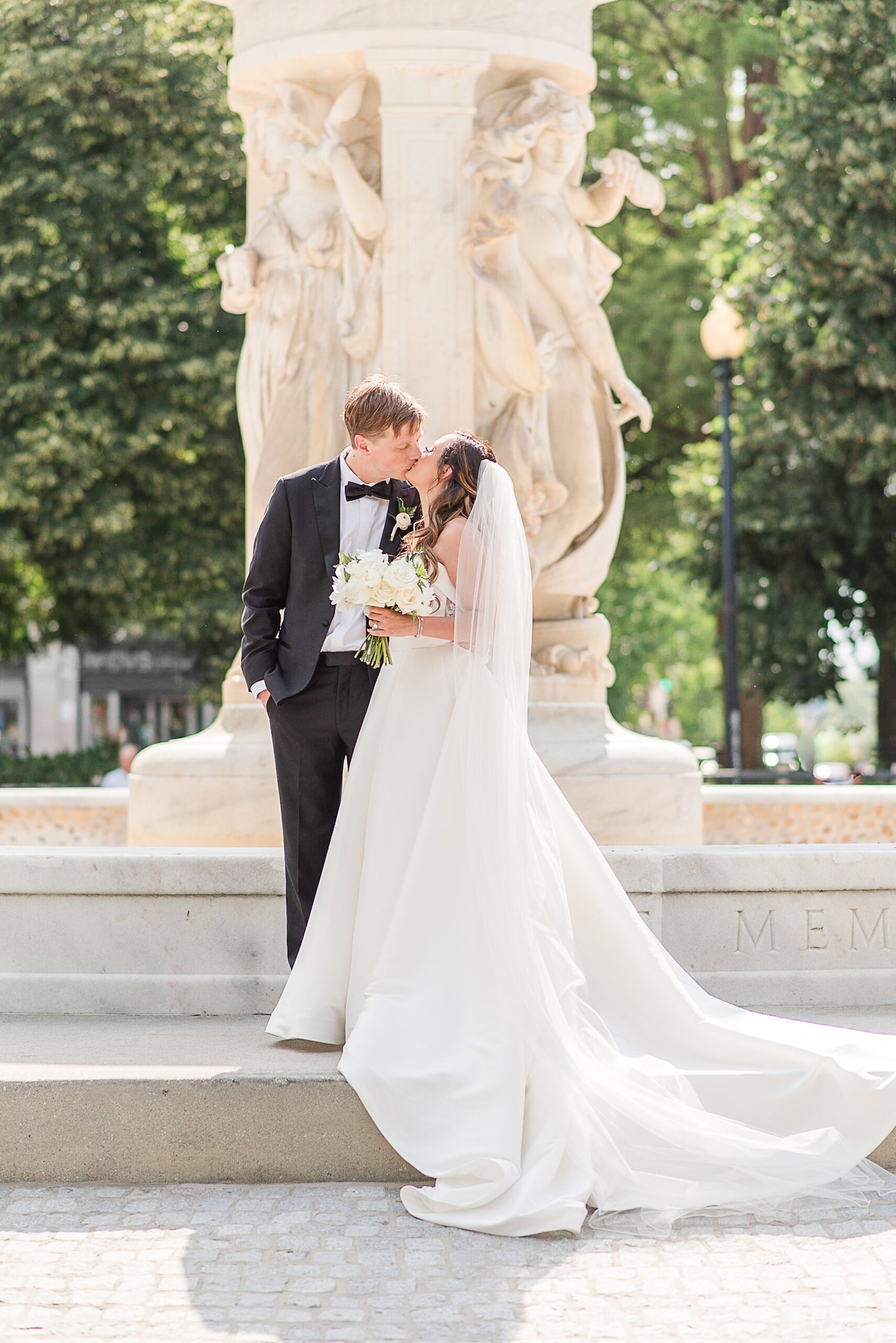 Newlyweds kiss while standing beside a tall fountain at one of the Wedding Venues In Maryland