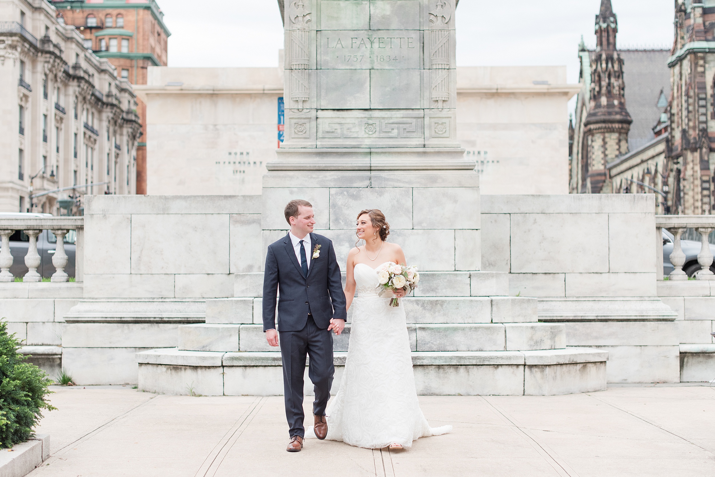 Newlyweds hold hands while walking by the Lafayette memorial to one of the fabulous Wedding Venues In Maryland
