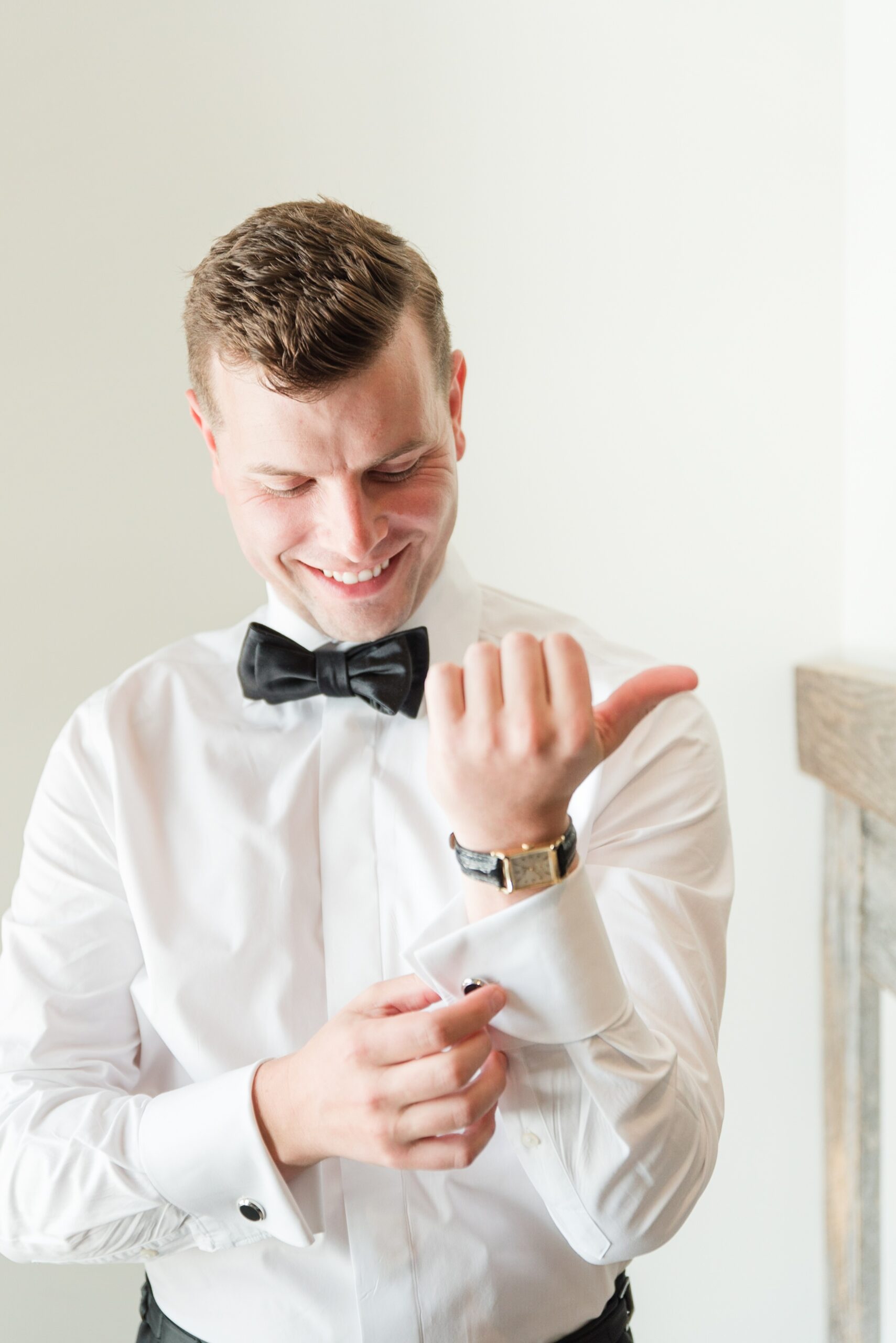 A groom buttons his cuff while getting ready for his wedding without his jacket