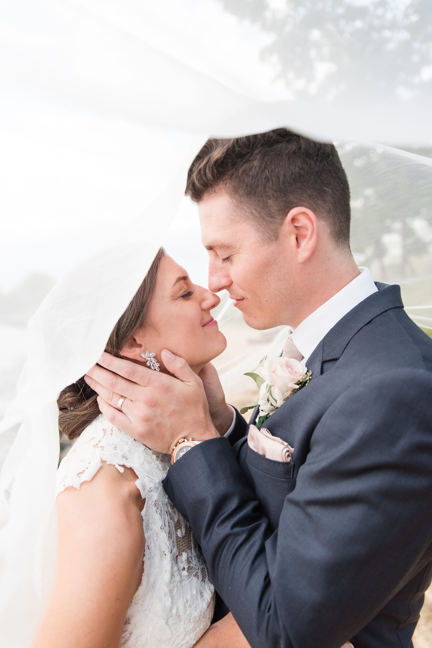 Newlyweds lean in for a happy kiss while hiding under a large veil outside during their William Paca House Wedding