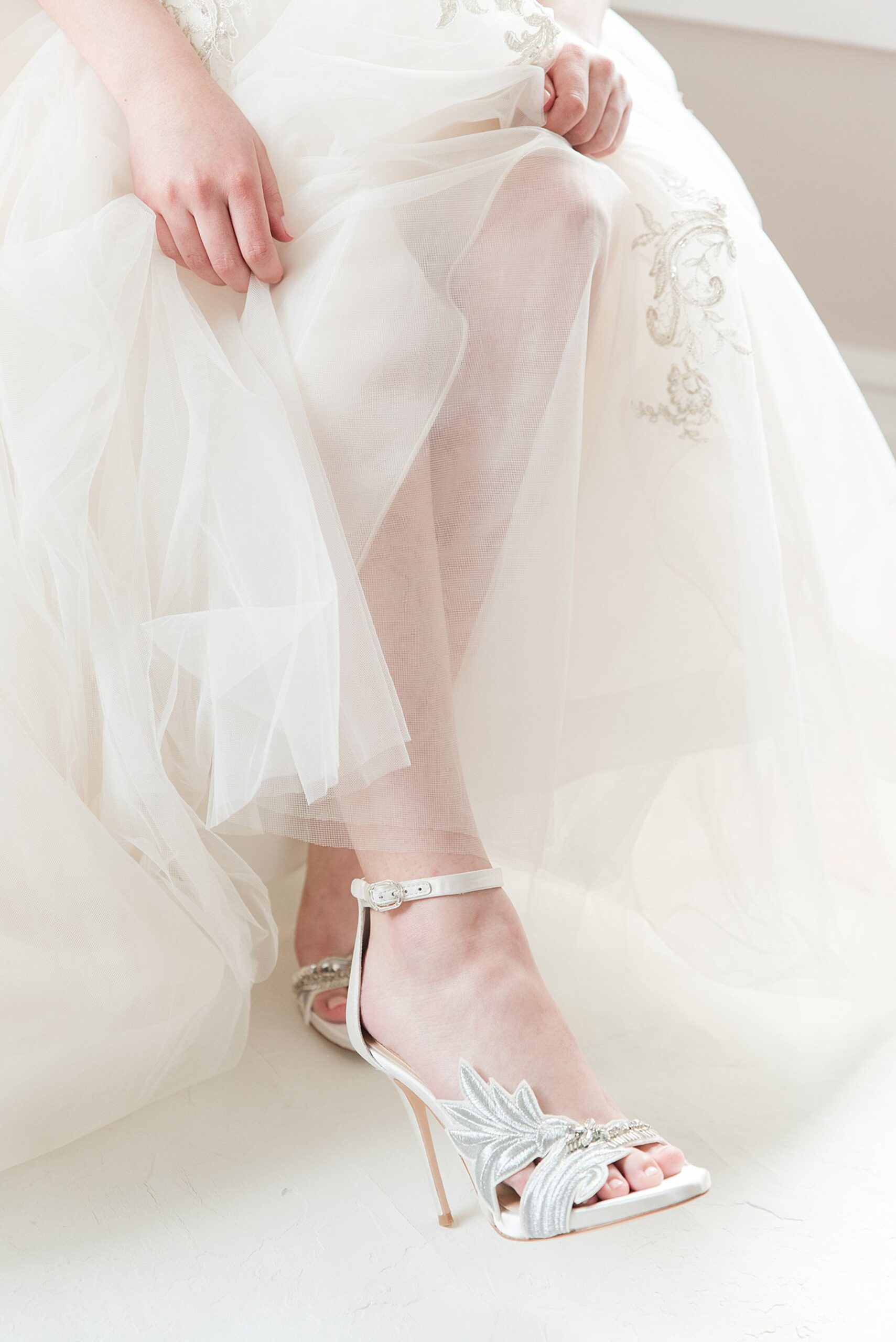 A bride sits in a chair while showing off her ornate shoes under her dress at her William Paca House Wedding